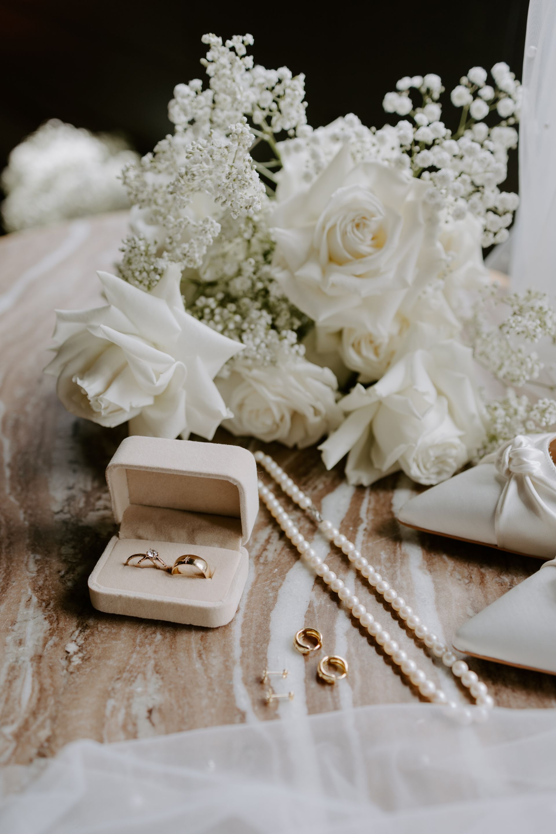 White bridal bouquet with gold rings and pearl necklace on a soft fabric backdrop