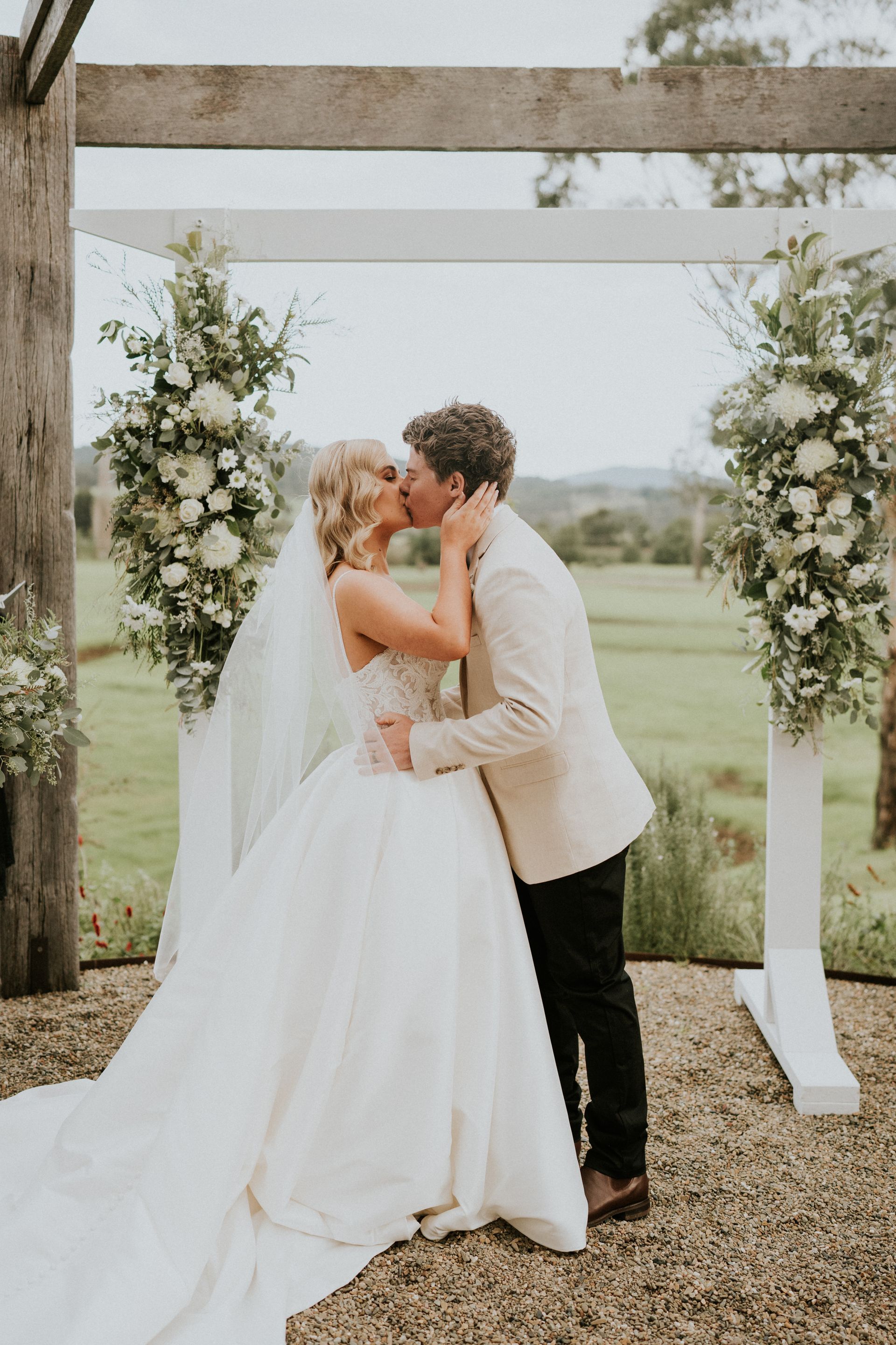 Bride and groom kissing under a floral wedding arch outdoors