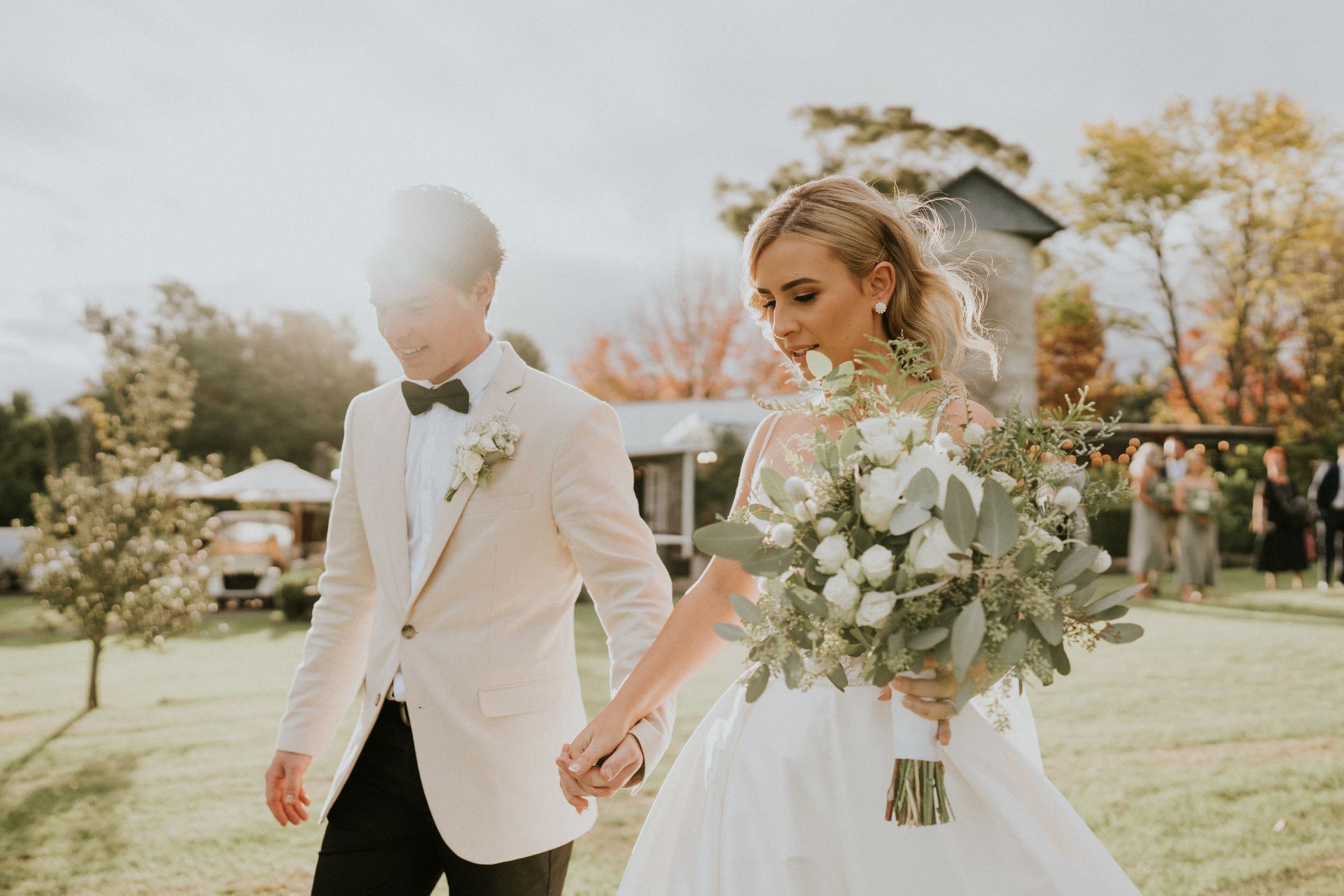Bride and groom in white holding hands outdoors at a sunny wedding ceremony