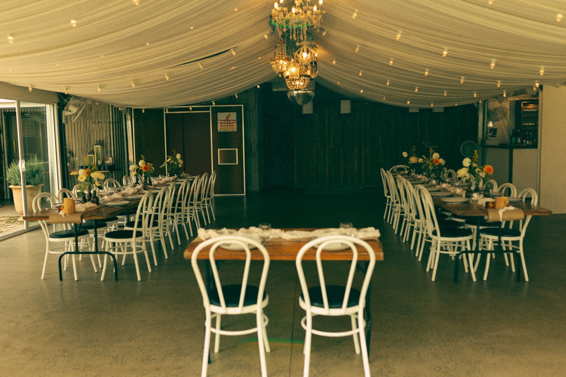 Elegant banquet hall with white chairs, round tables, and draped ceiling under soft chandelier lights