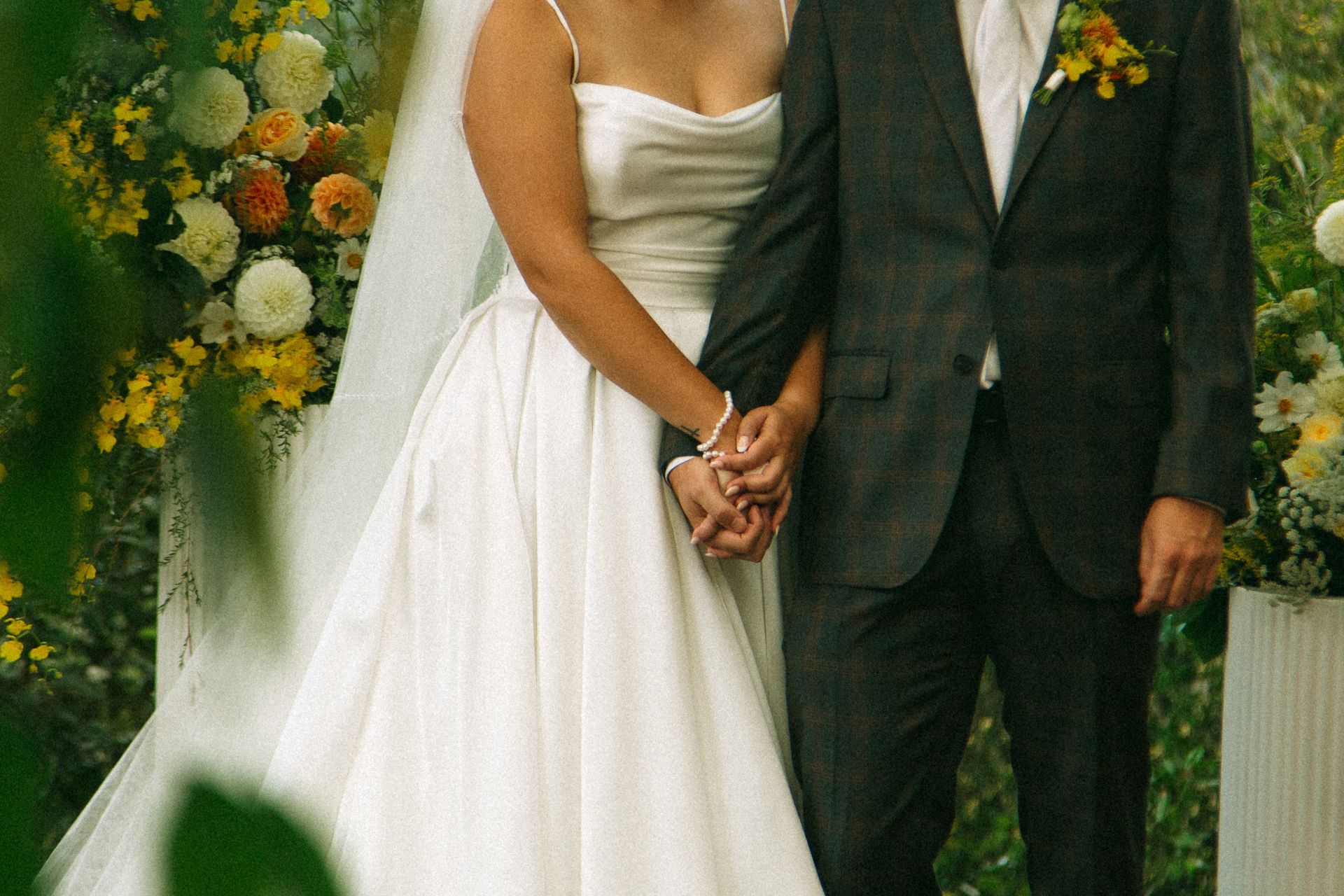Bride and groom holding hands at an outdoor wedding ceremony with floral arrangements