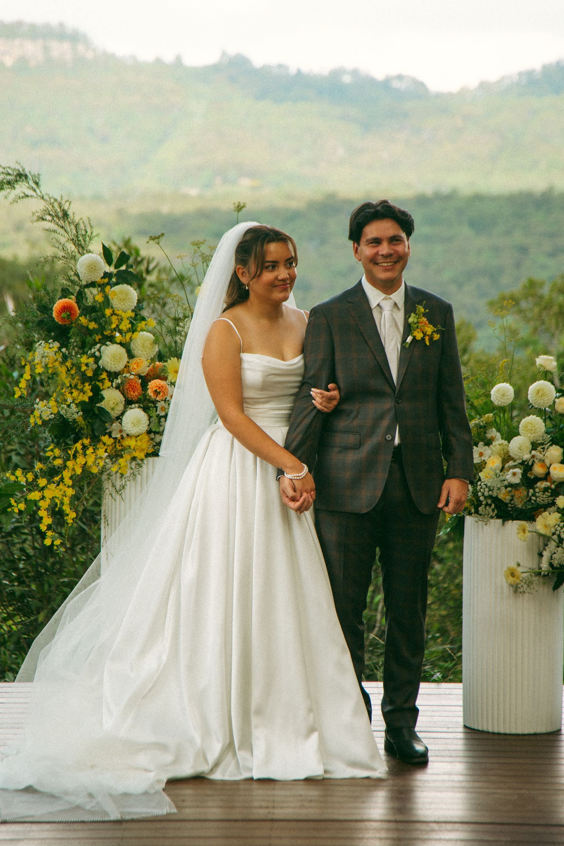Bride and groom standing together at an outdoor wedding with floral decorations and mountain views