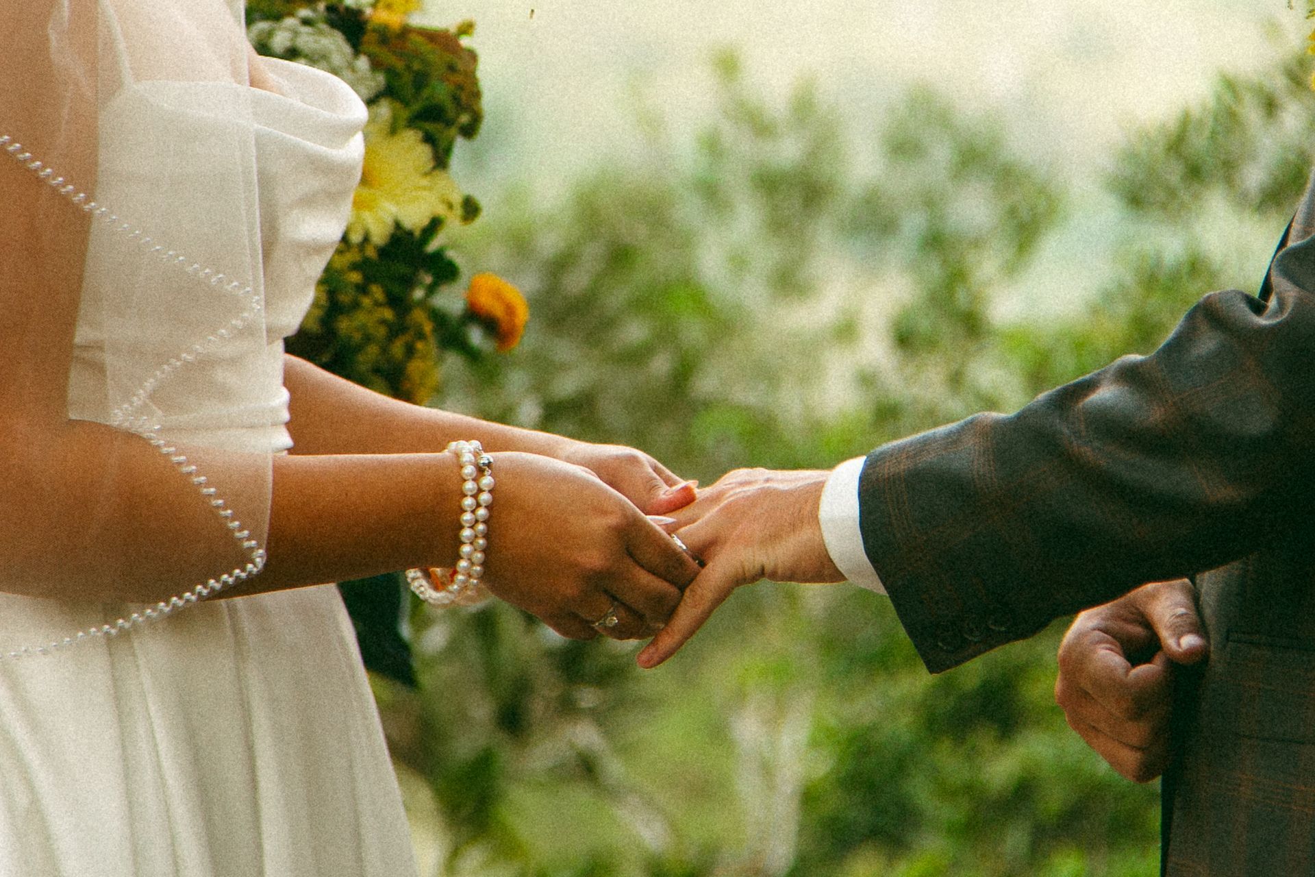 Two people holding hands during an outdoor wedding ceremony, with flowers in the background