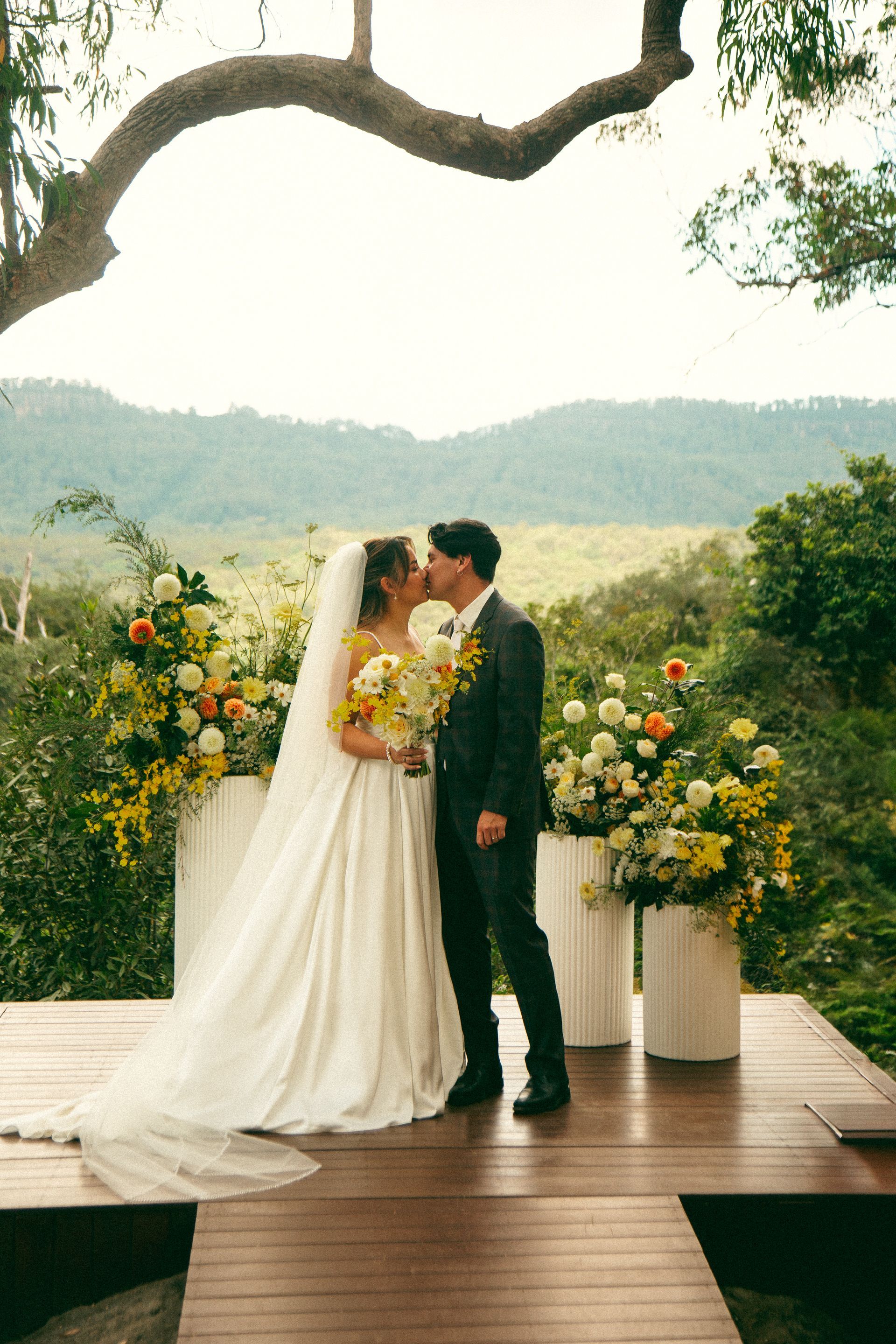 Bride and groom kissing at an outdoor wedding altar with flowers and hillside views