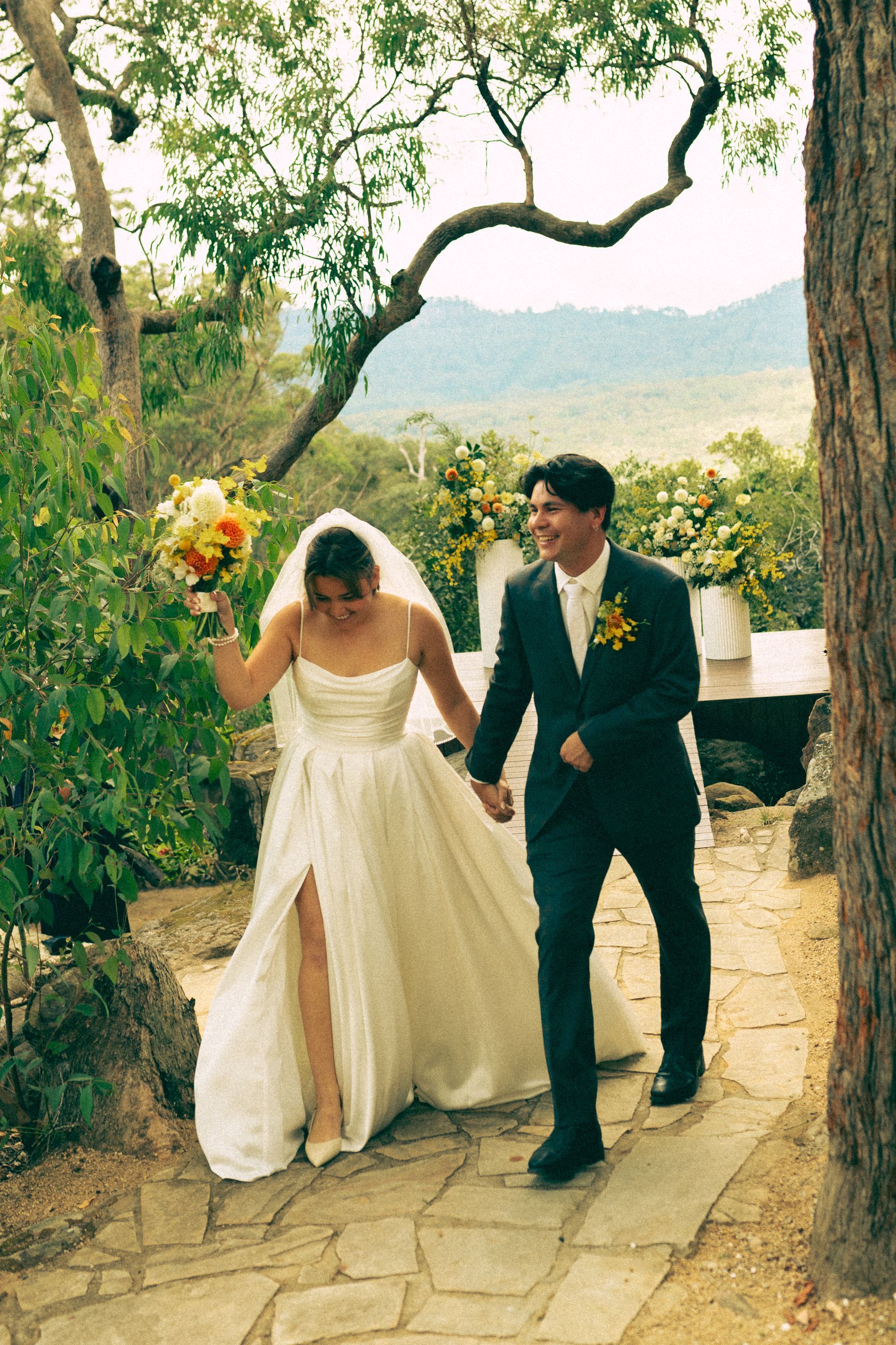 Bride and groom walking hand in hand down a stone path in a rustic outdoor setting
