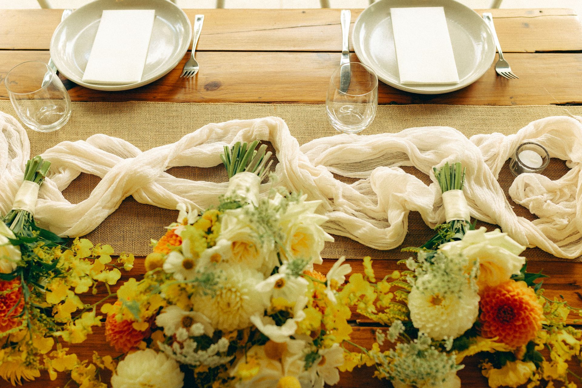 Flower-covered table with white plates, glassware, and woven white fabric in a rustic setting