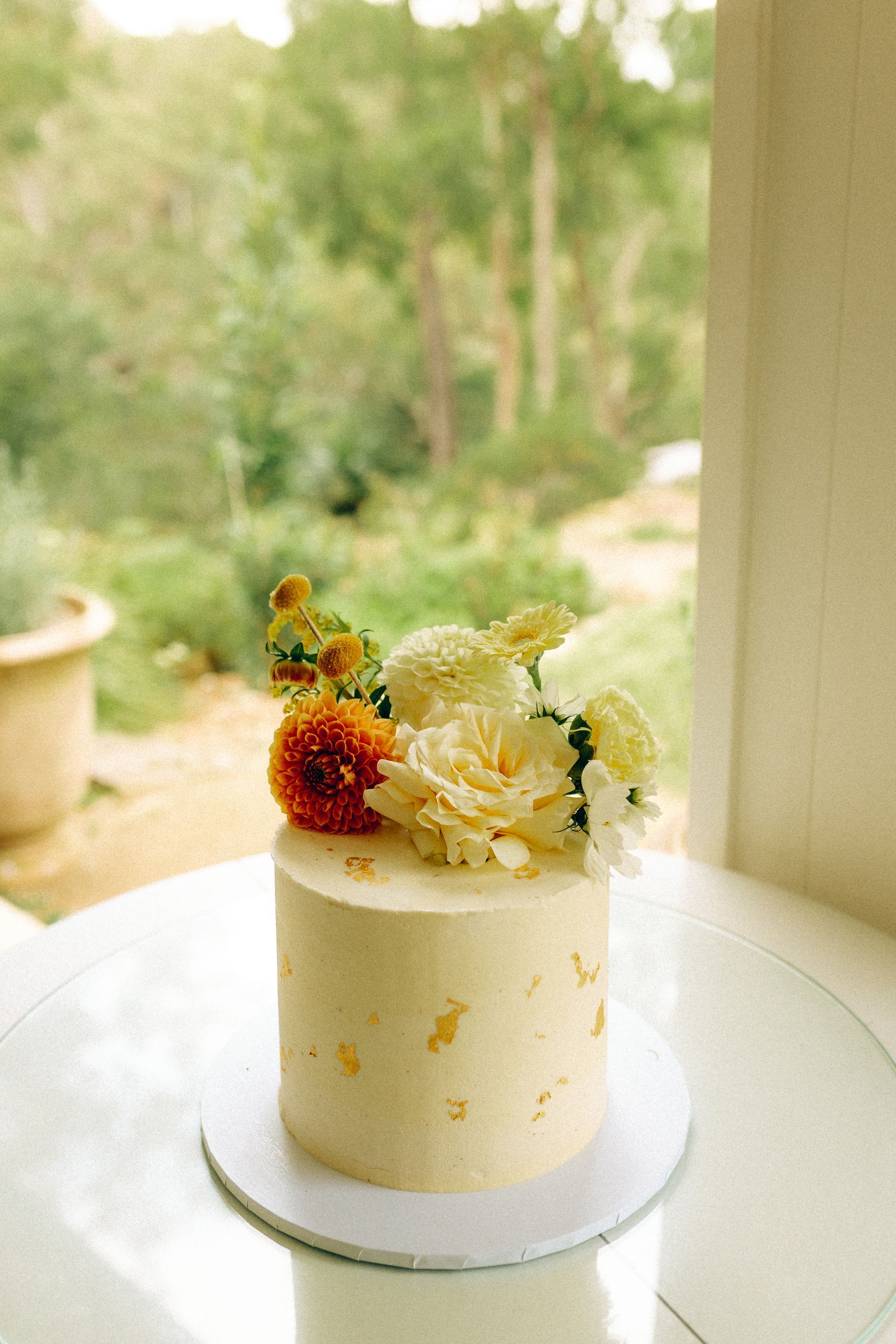 Small white cake topped with berries and cream on a table by a bright window