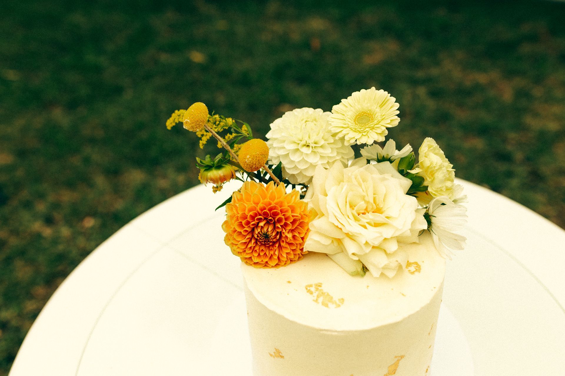 White floral arrangement with orange and yellow flowers in a cream vase on a table
