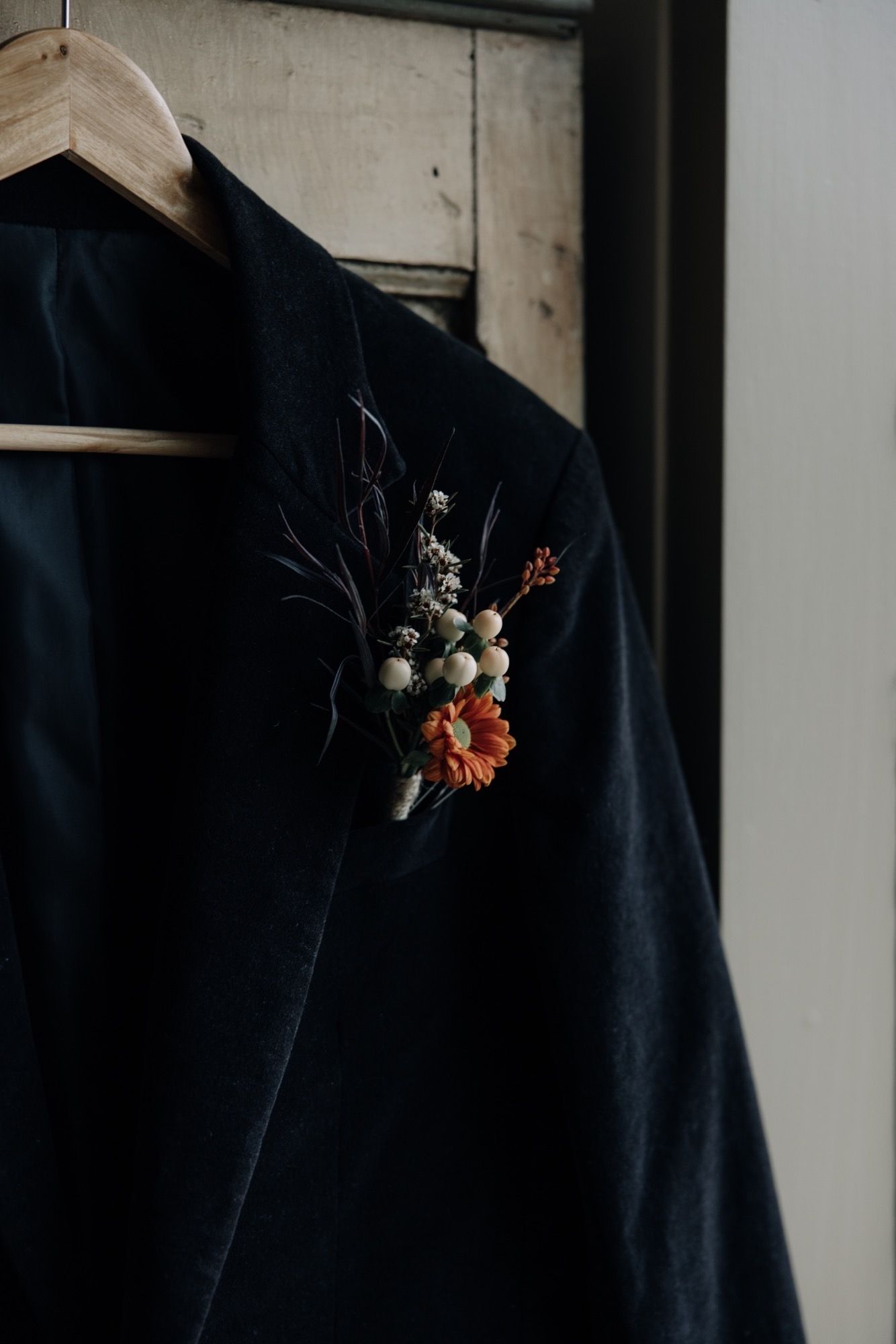 Navy blue blazer with a floral boutonniere hanging on a wooden hanger.