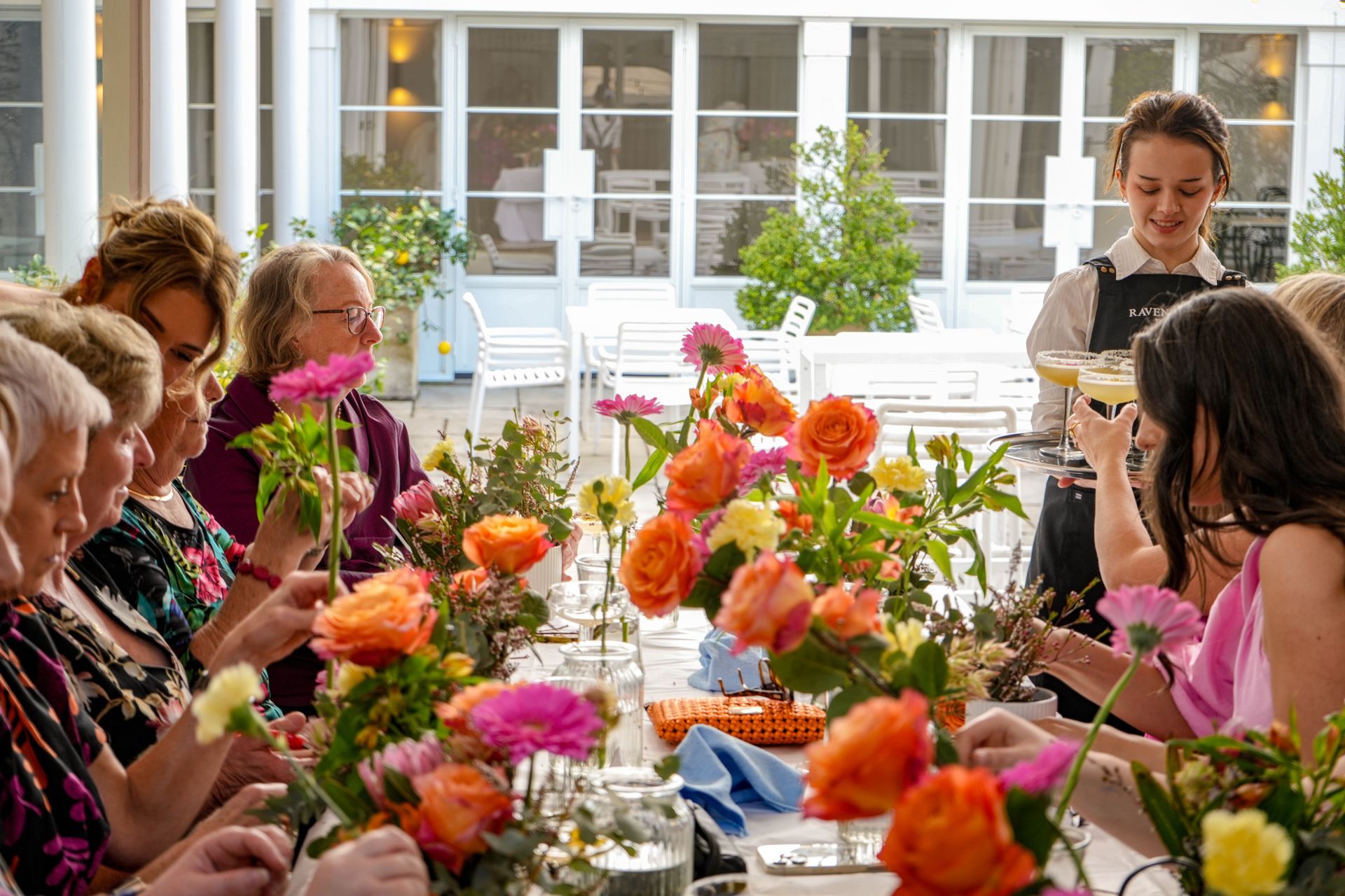People arranging colorful flower bouquets at a table in a bright room