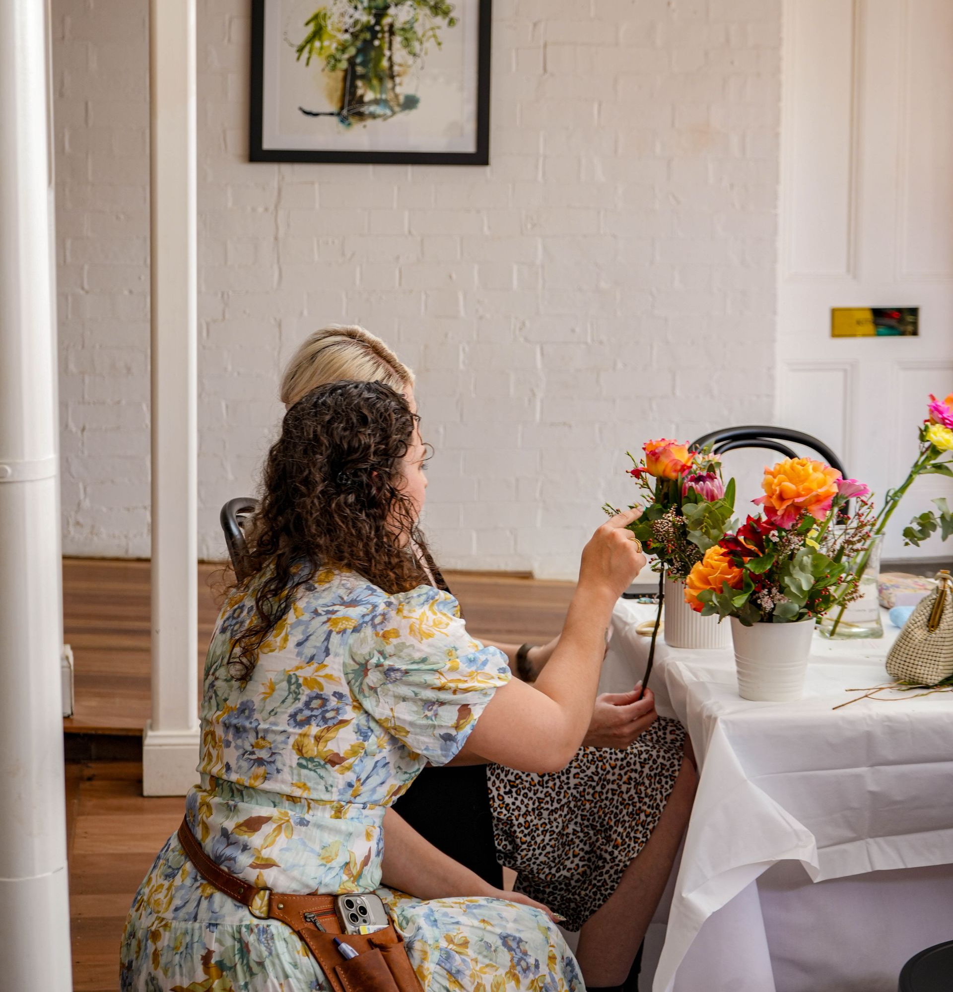 Two people arranging flowers at a white table in a bright room