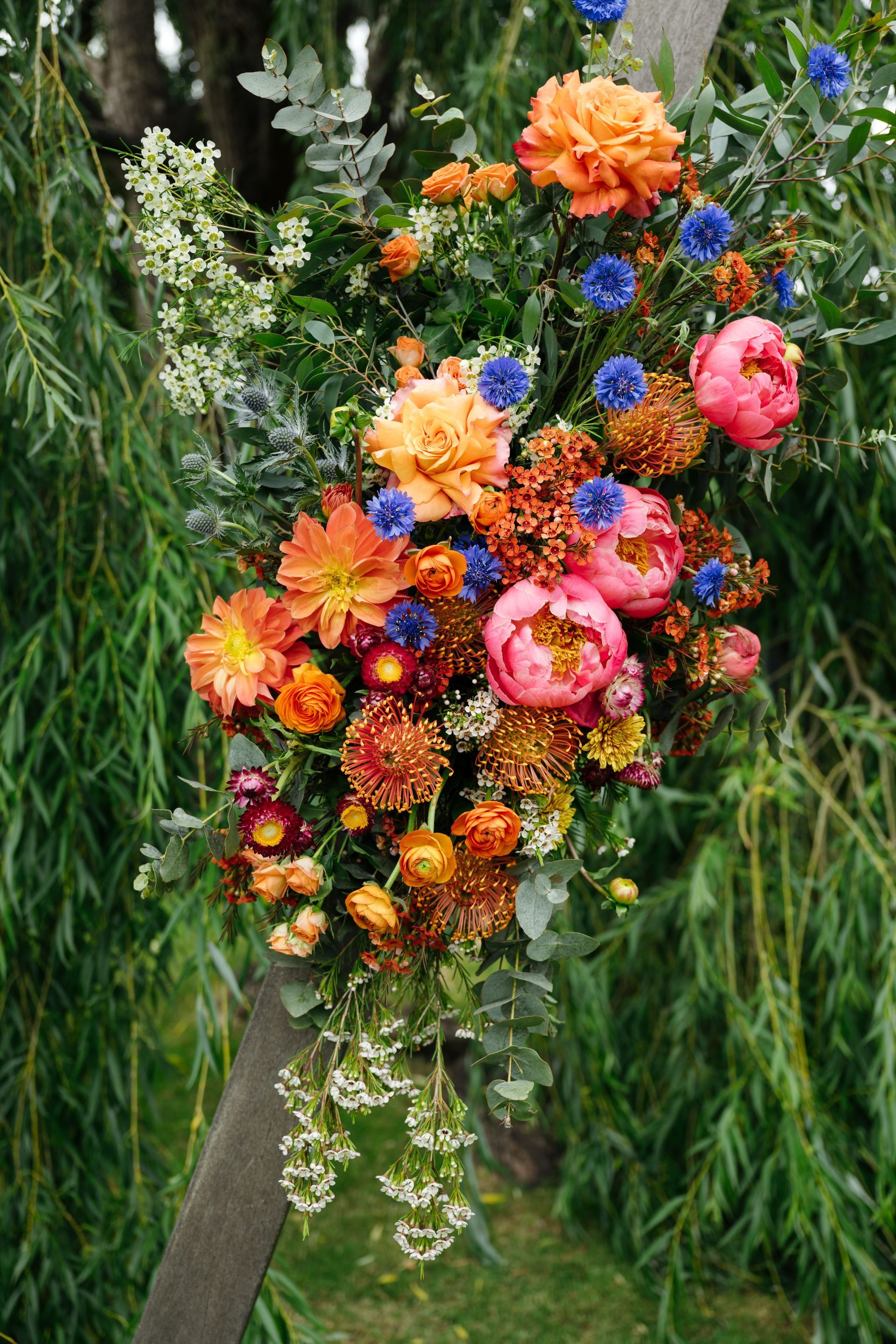 Colorful bouquet of orange, pink, and blue flowers arranged on a tree branch outdoors
