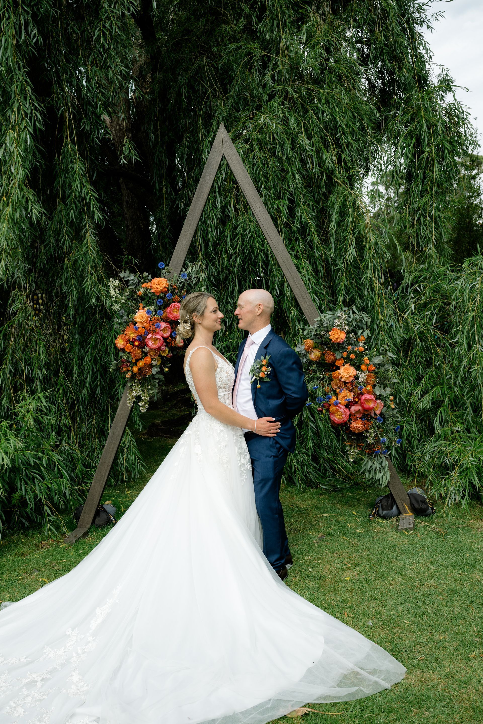 Bride and groom kissing under a floral wooden arch in a garden outdoors