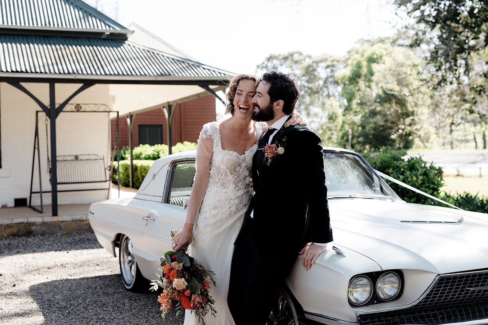 Couple kissing beside a white vintage car at an outdoor wedding venue