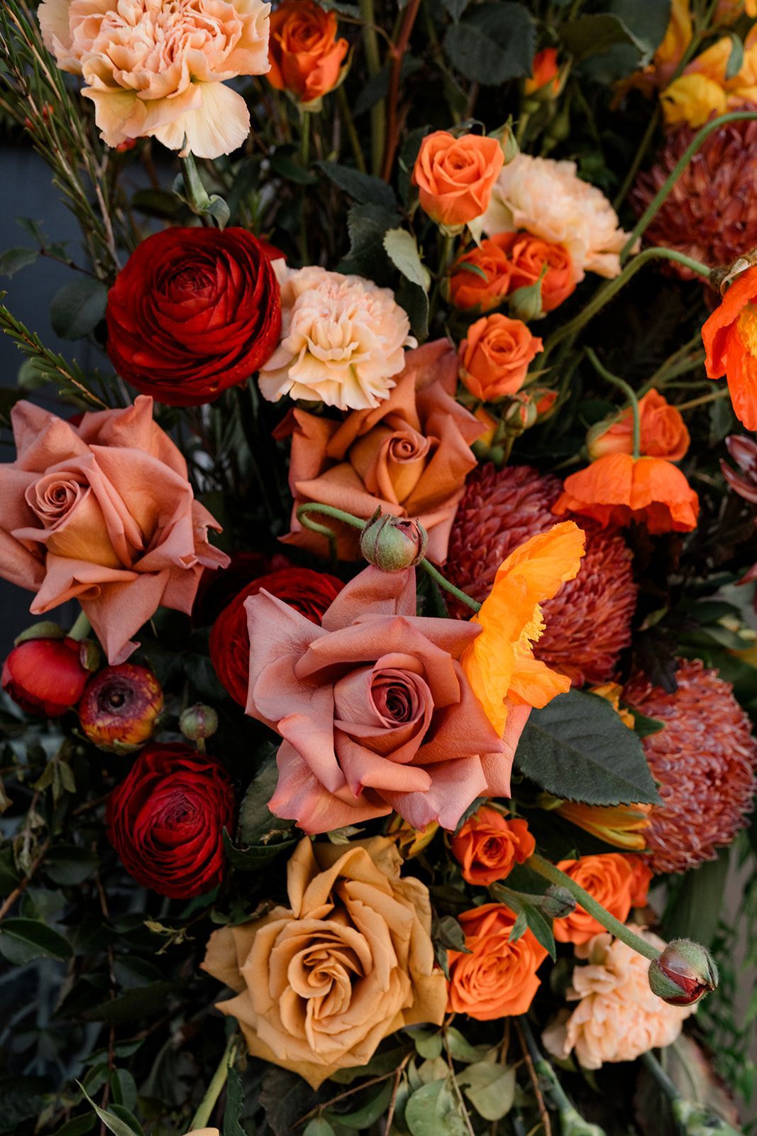 Assorted roses in warm pink, peach, red, and orange tones with green foliage