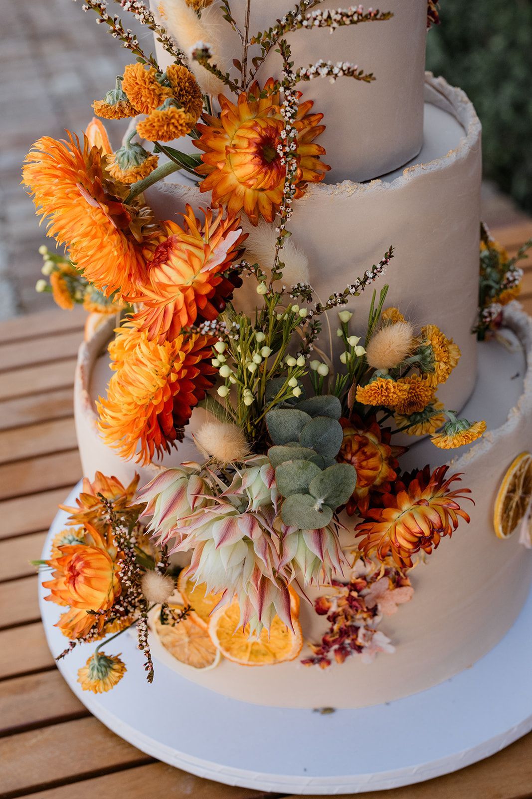 Three-tier white cake with orange and cream dried-flower decorations