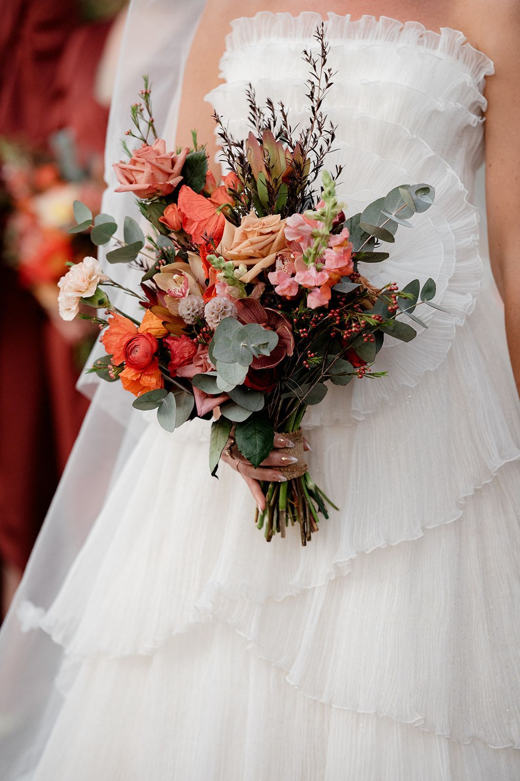 Bridal bouquet of coral, blush, and green flowers against a white wedding dress