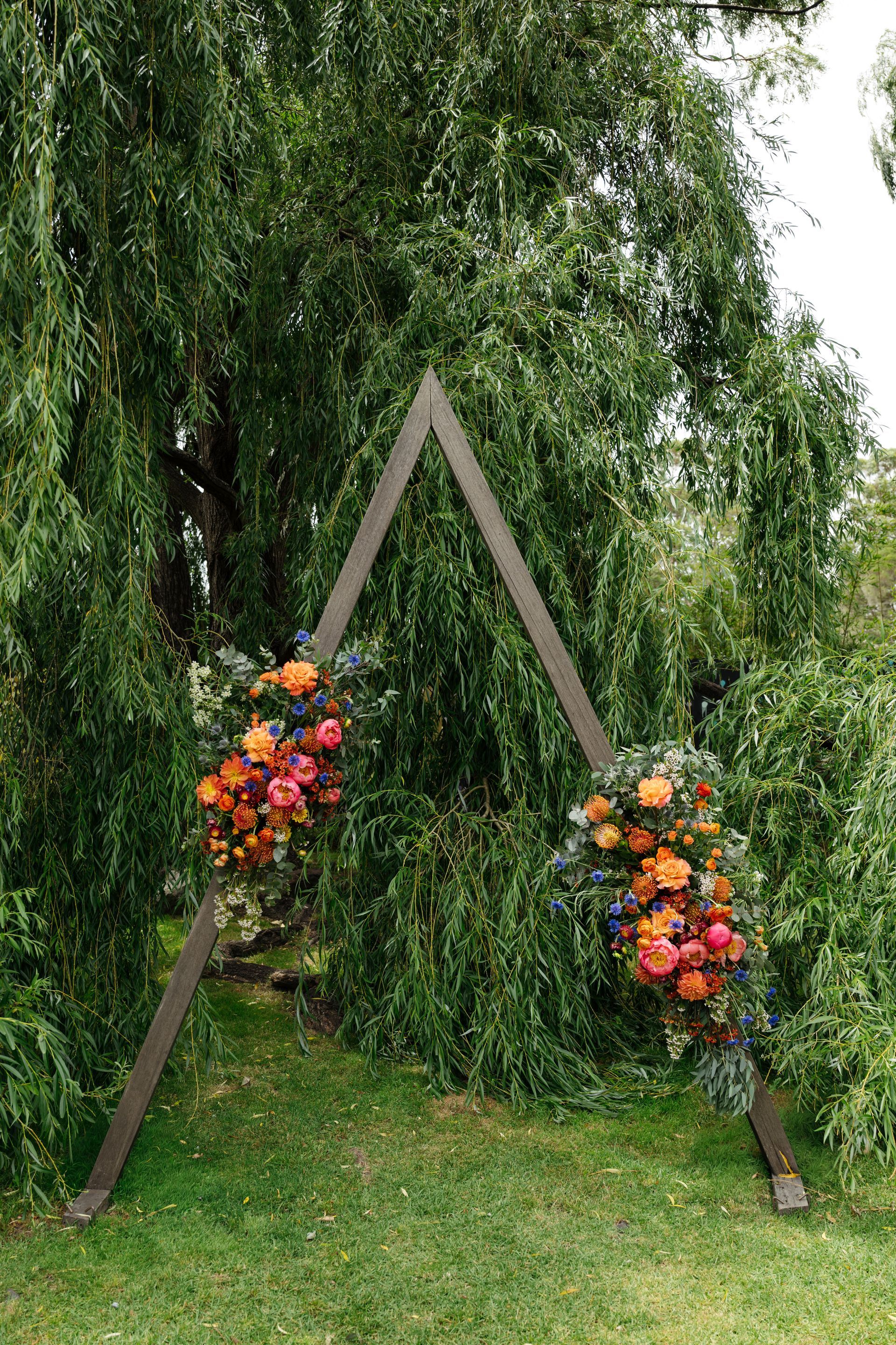 Wooden triangle arch with colorful flower arrangements on a grassy outdoor lawn