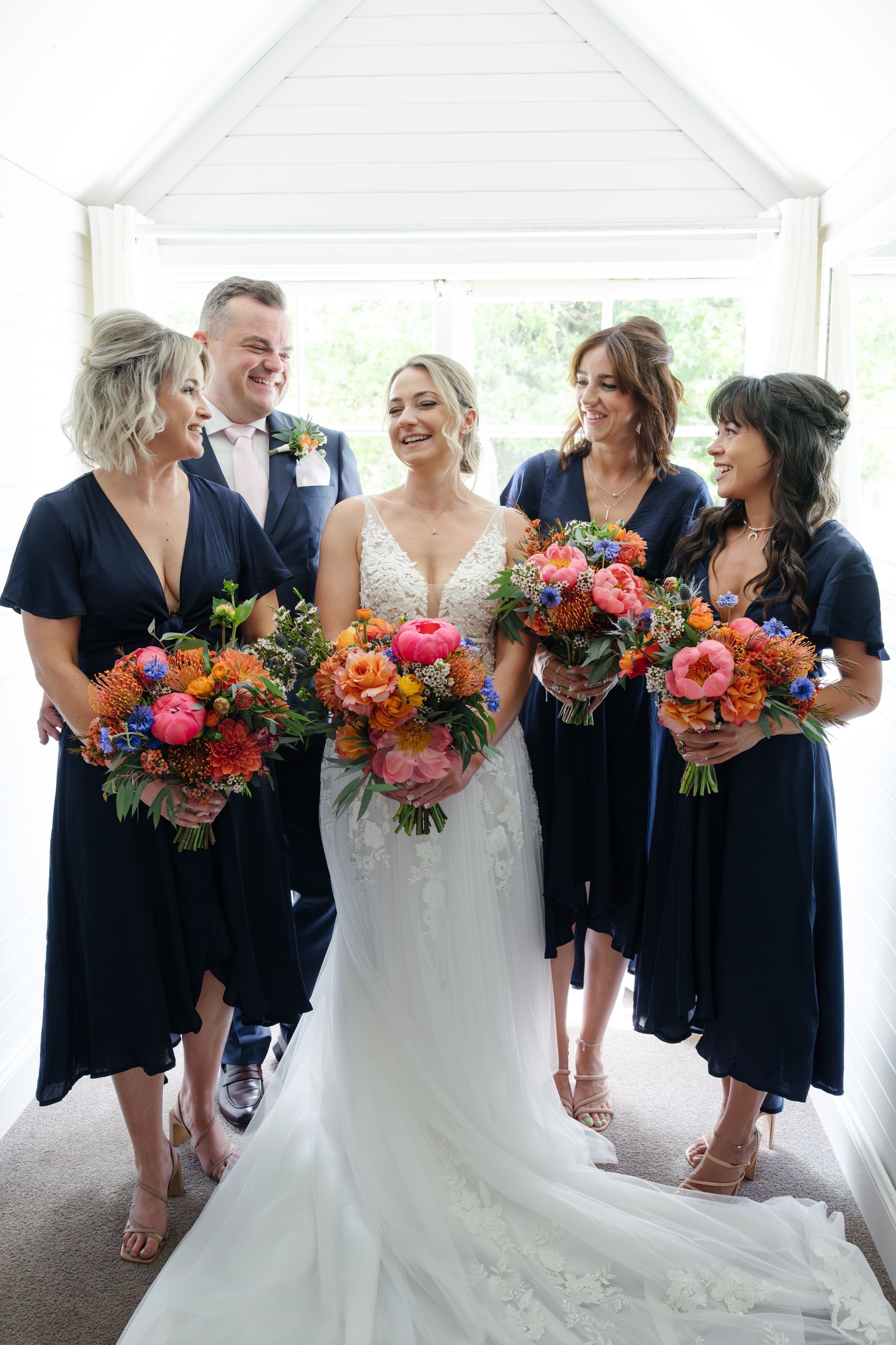 Wedding party posing in a bright doorway, holding colorful bouquets.