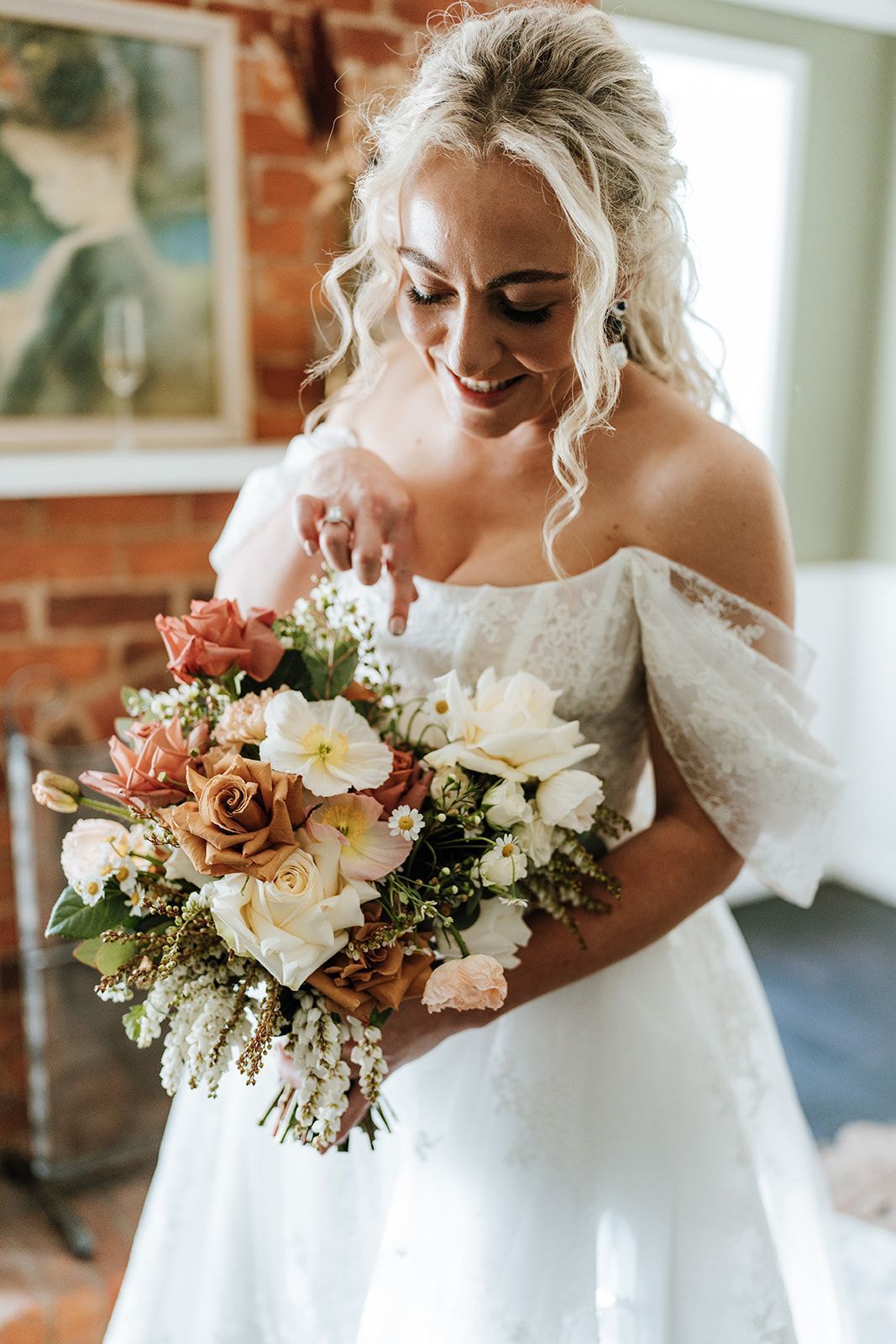 Bride in an off-shoulder white gown holding a colorful bouquet and smiling indoors