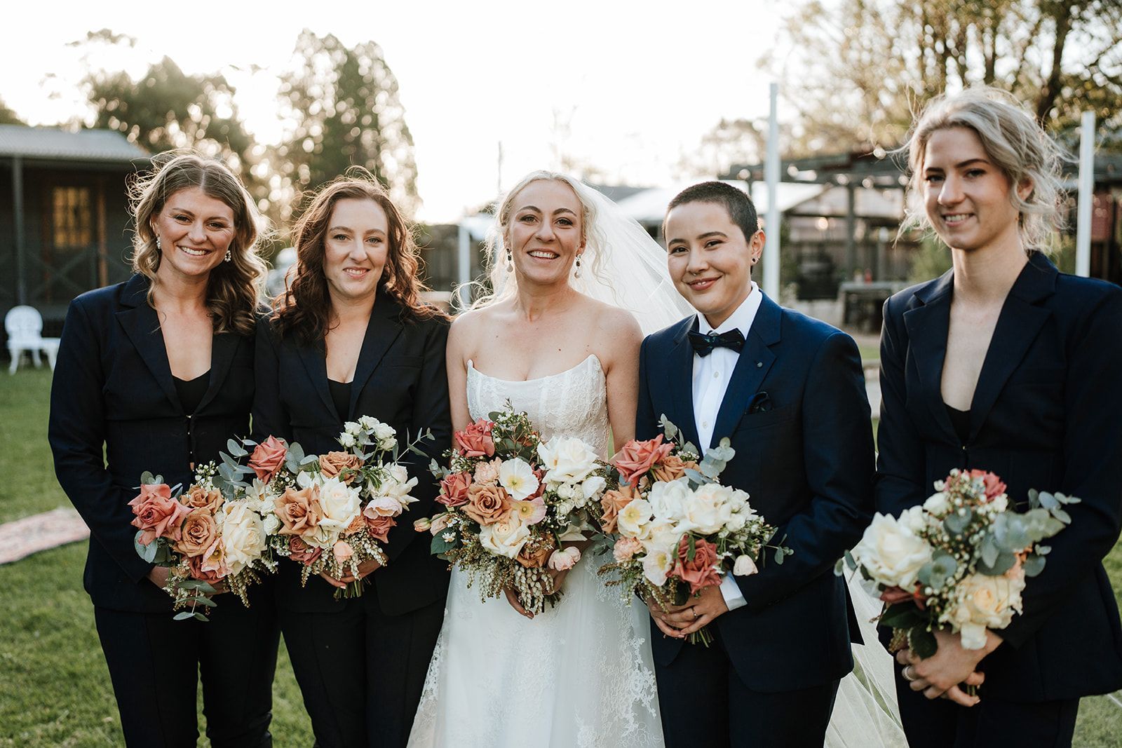 Bride and four wedding party members holding bouquets outdoors at sunset