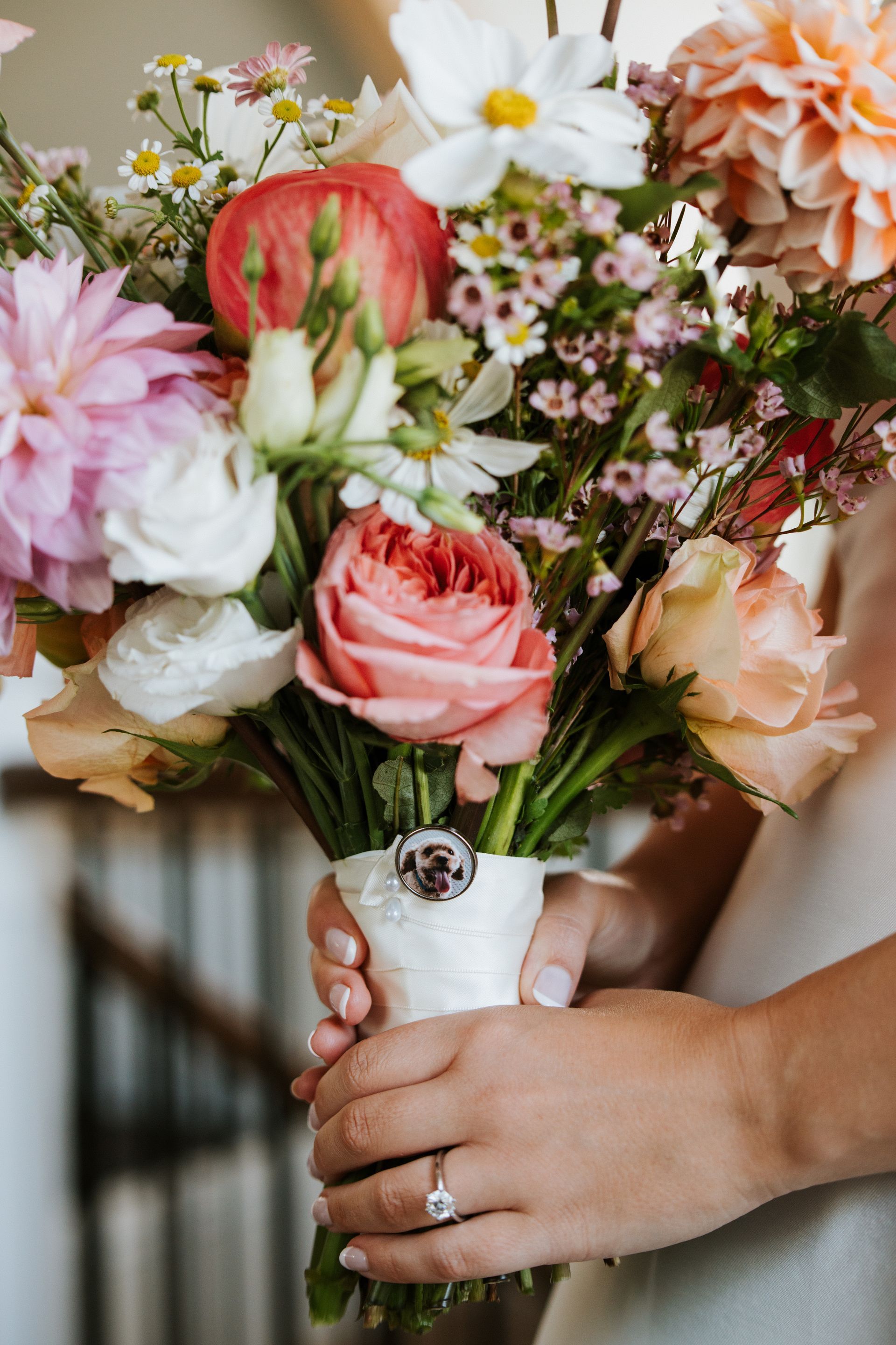 Hands holding a white vase of pink and white flowers