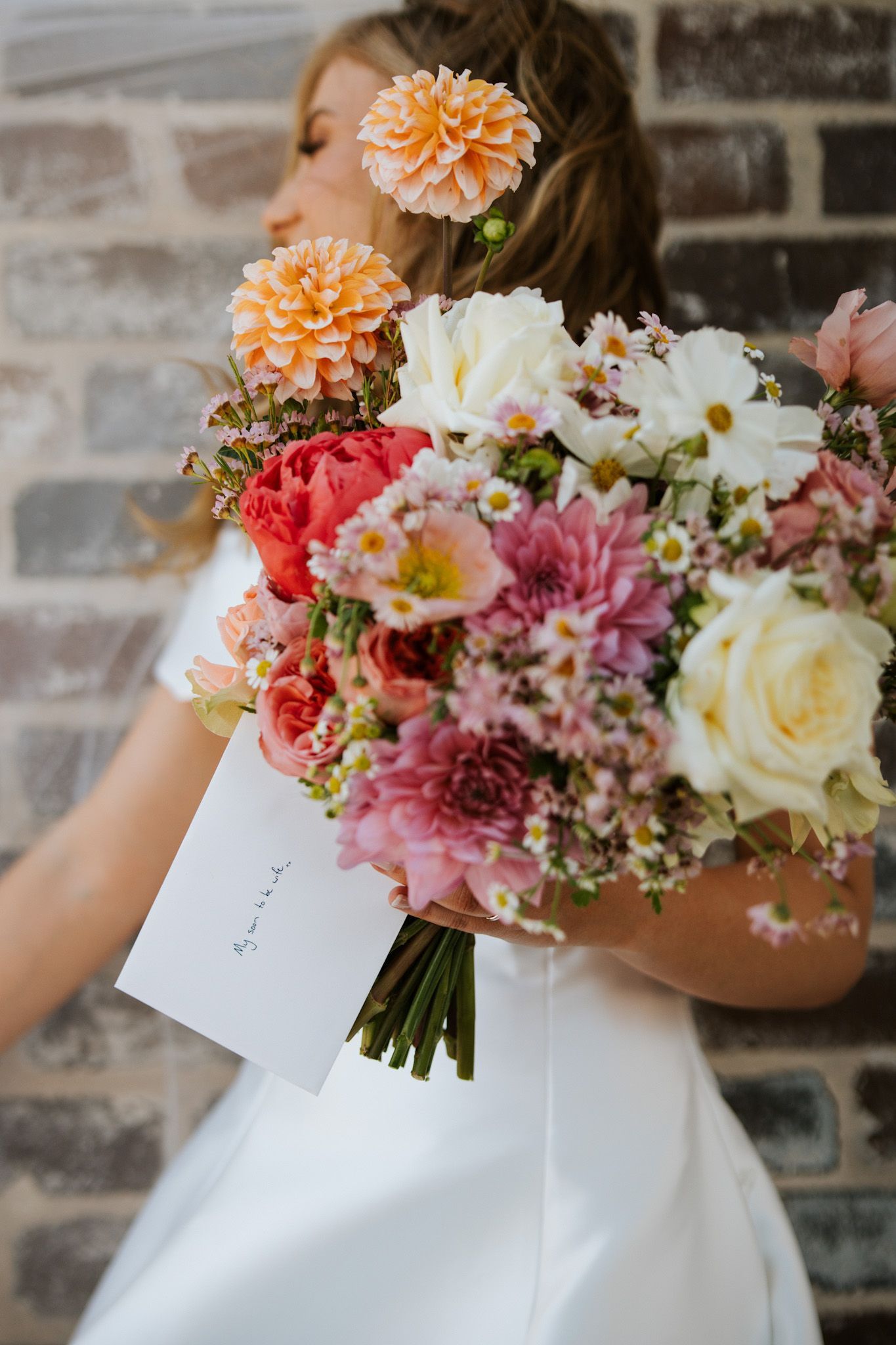 Bride in white dress holding a large colorful bouquet in front of a stone wall