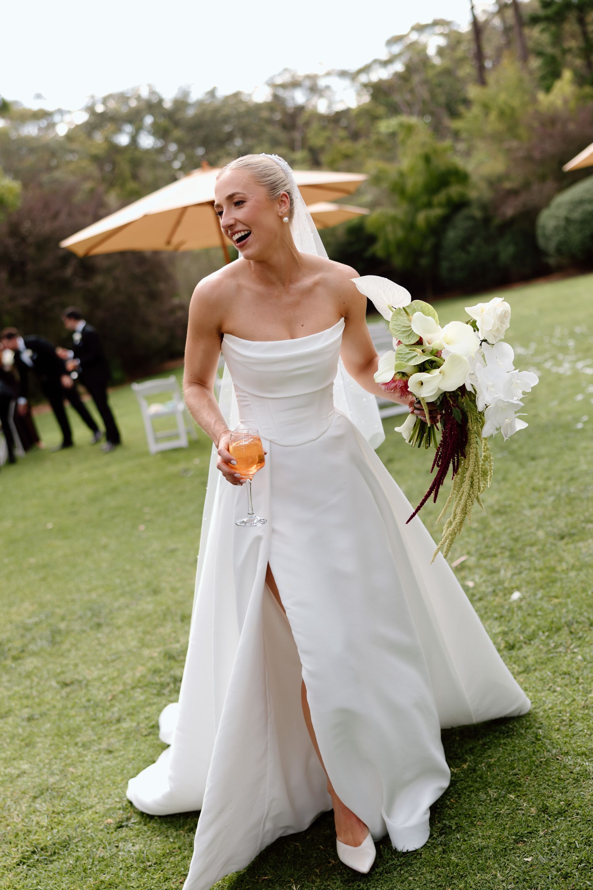 Bride in a white wedding dress holding a bouquet and drink outdoors at a garden wedding