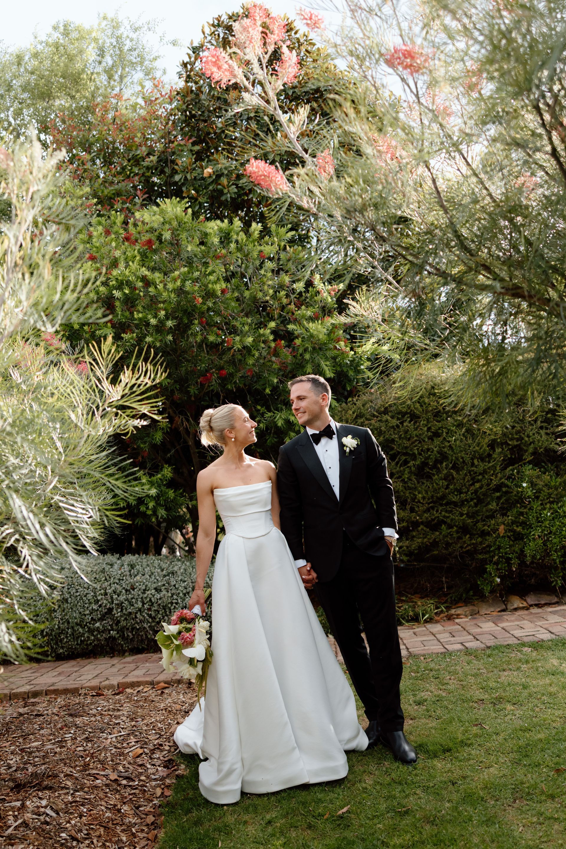 Bride and groom in wedding attire standing in a garden with greenery and flowers