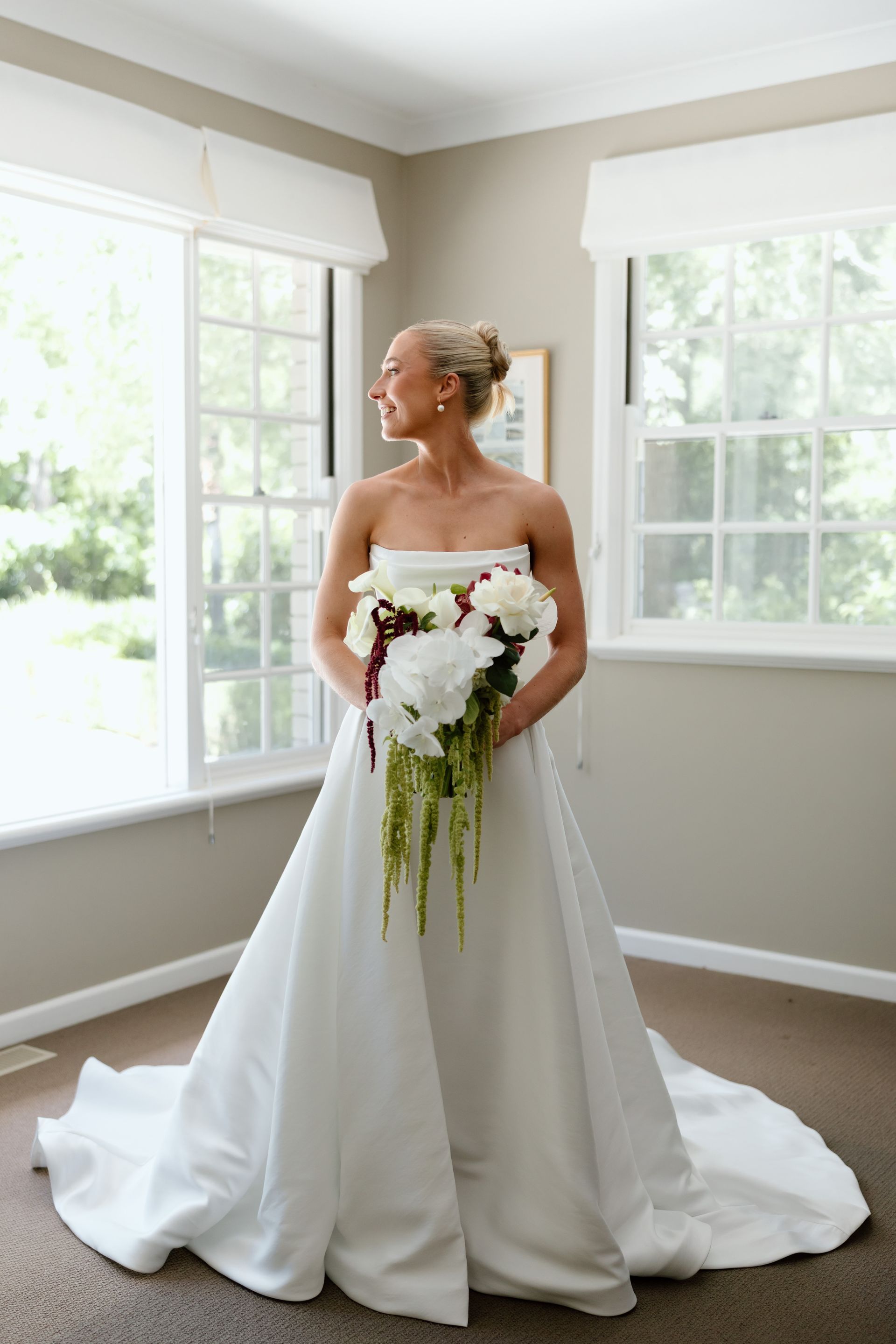 Bride in a white gown holding a cascading bouquet by bright windows