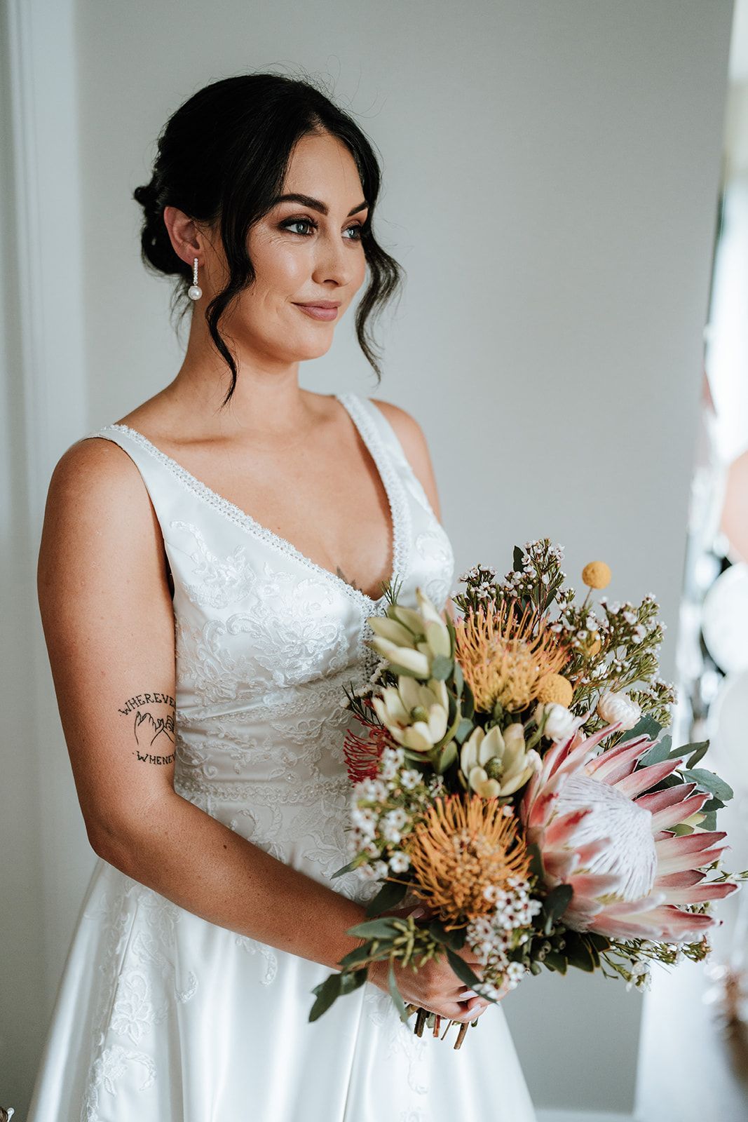 Bride in a white satin dress holding a bouquet of pastel flowers indoors