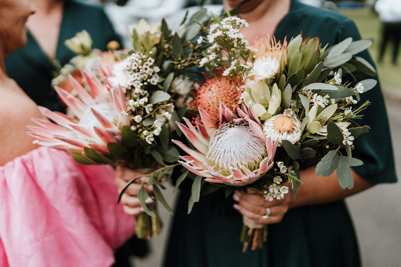 Person holding a pink and green bouquet with protea flowers in a formal outdoor setting