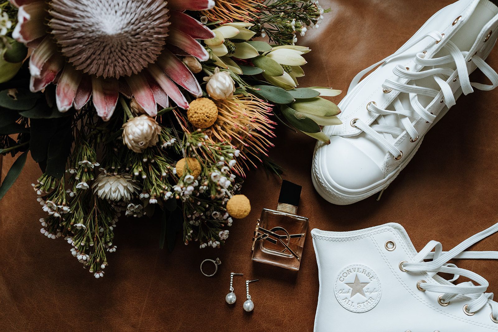 White sneakers beside a floral bouquet and jewelry on a brown surface