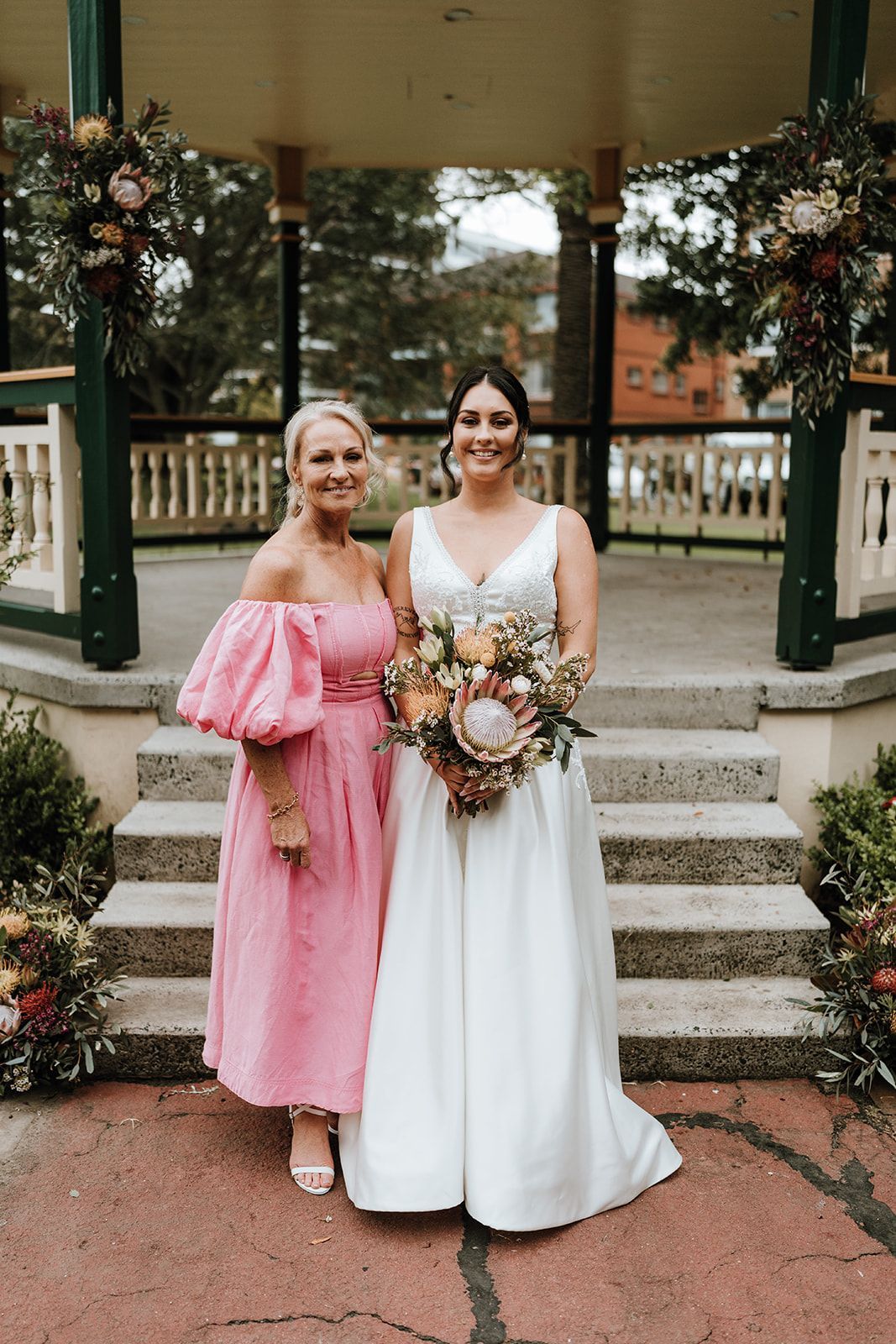 Two women in pink and white dresses holding bouquets on a gazebo staircase outdoors