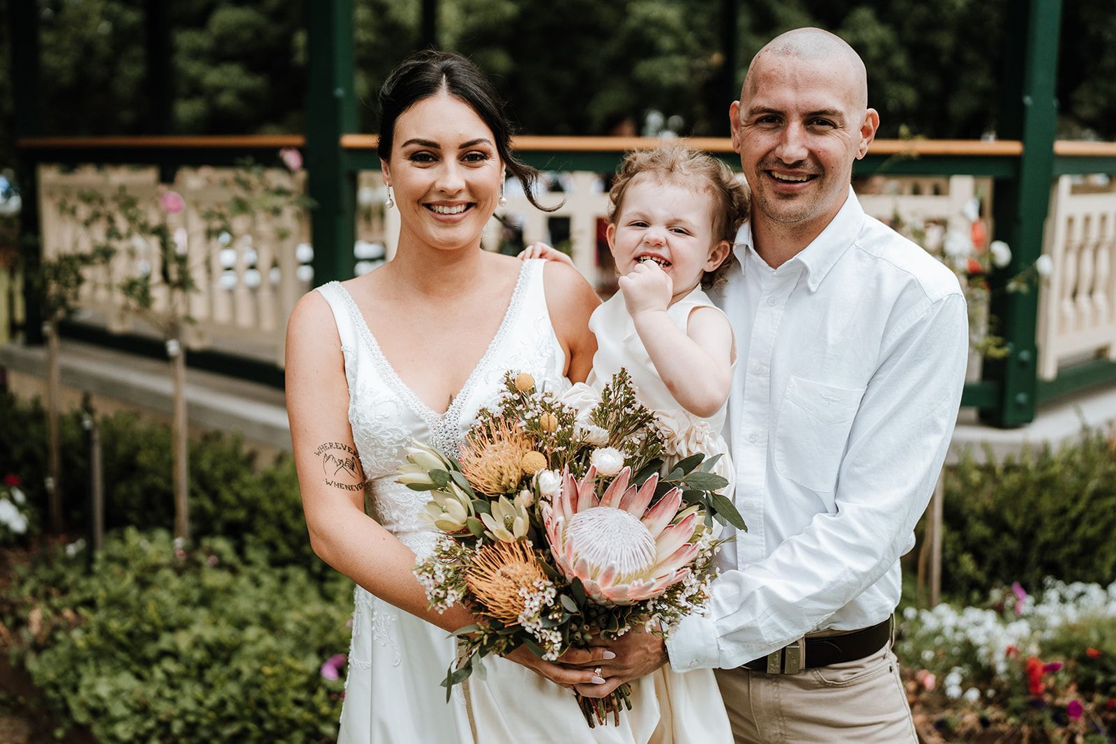 Three people posing outdoors in a garden, holding a bouquet and smiling