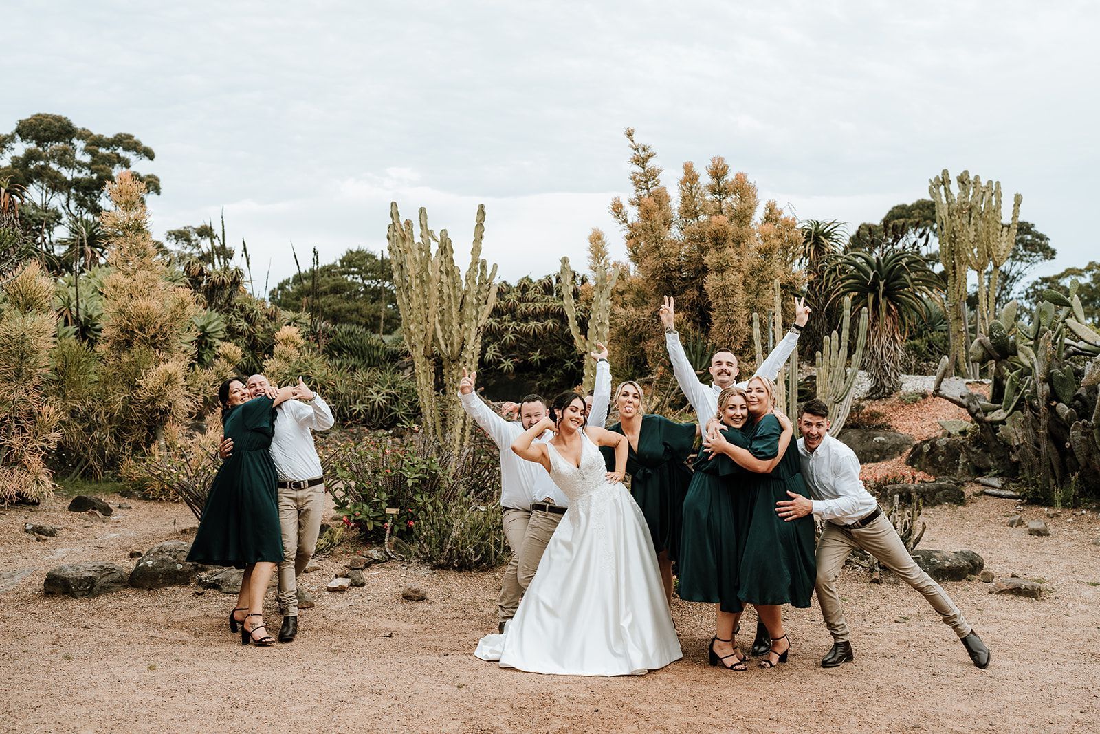 Group of friends posing in a desert garden, with a bride in a white dress holding up a bouquet.