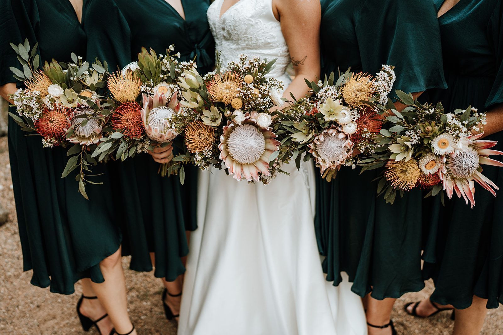 Bridal party holding cascading bouquets, with a white wedding dress centered among dark green dresses.
