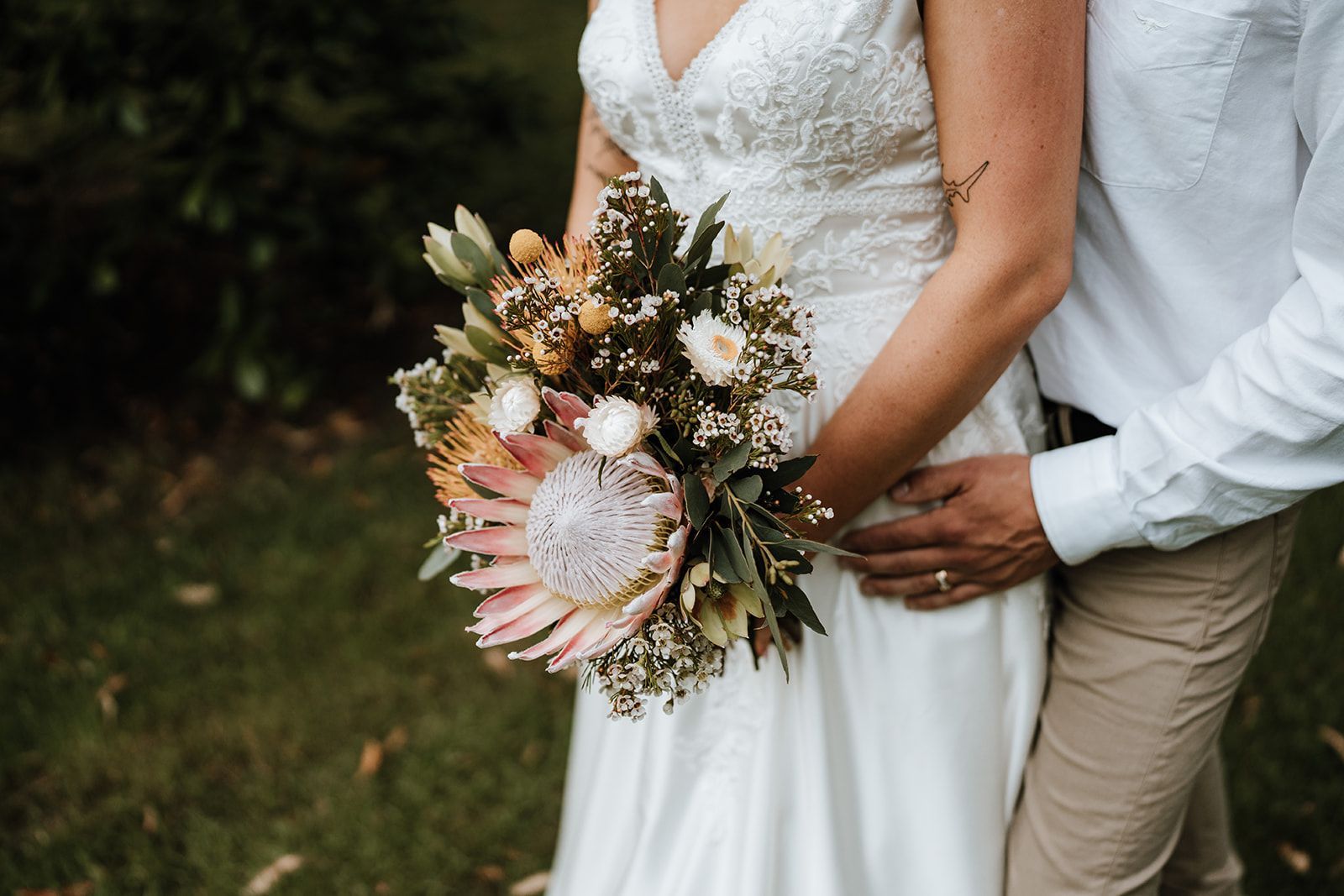 Wedding couple holding a bouquet, with the bride in a white dress outdoors.
