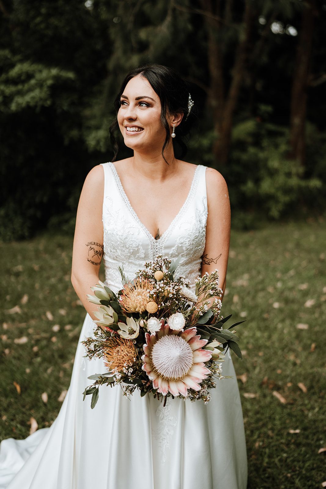 Bride in a white dress holding a bouquet, standing outdoors in a garden.