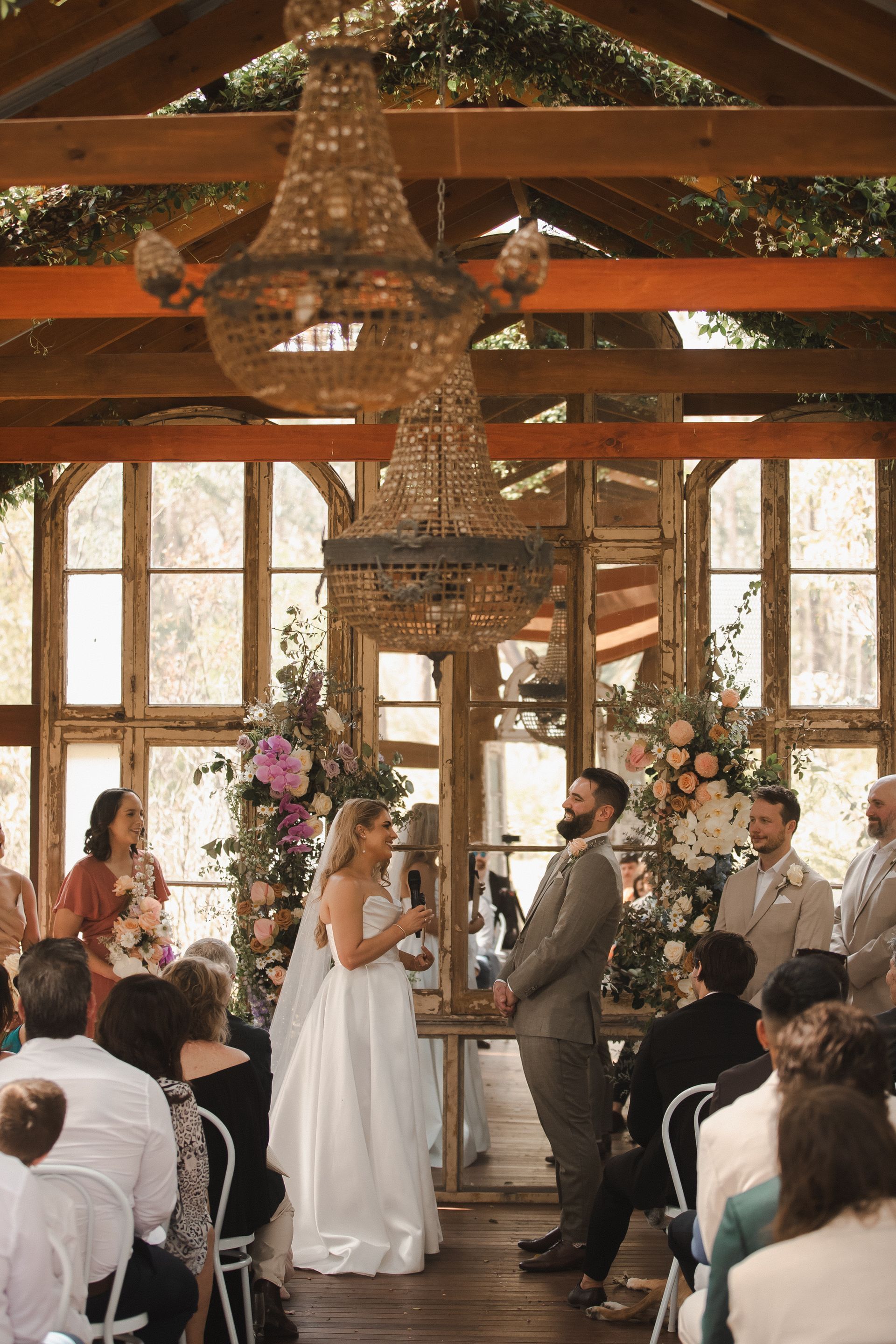 Wedding couple exchanging vows under a wooden chandelier in a rustic, flower-decorated chapel