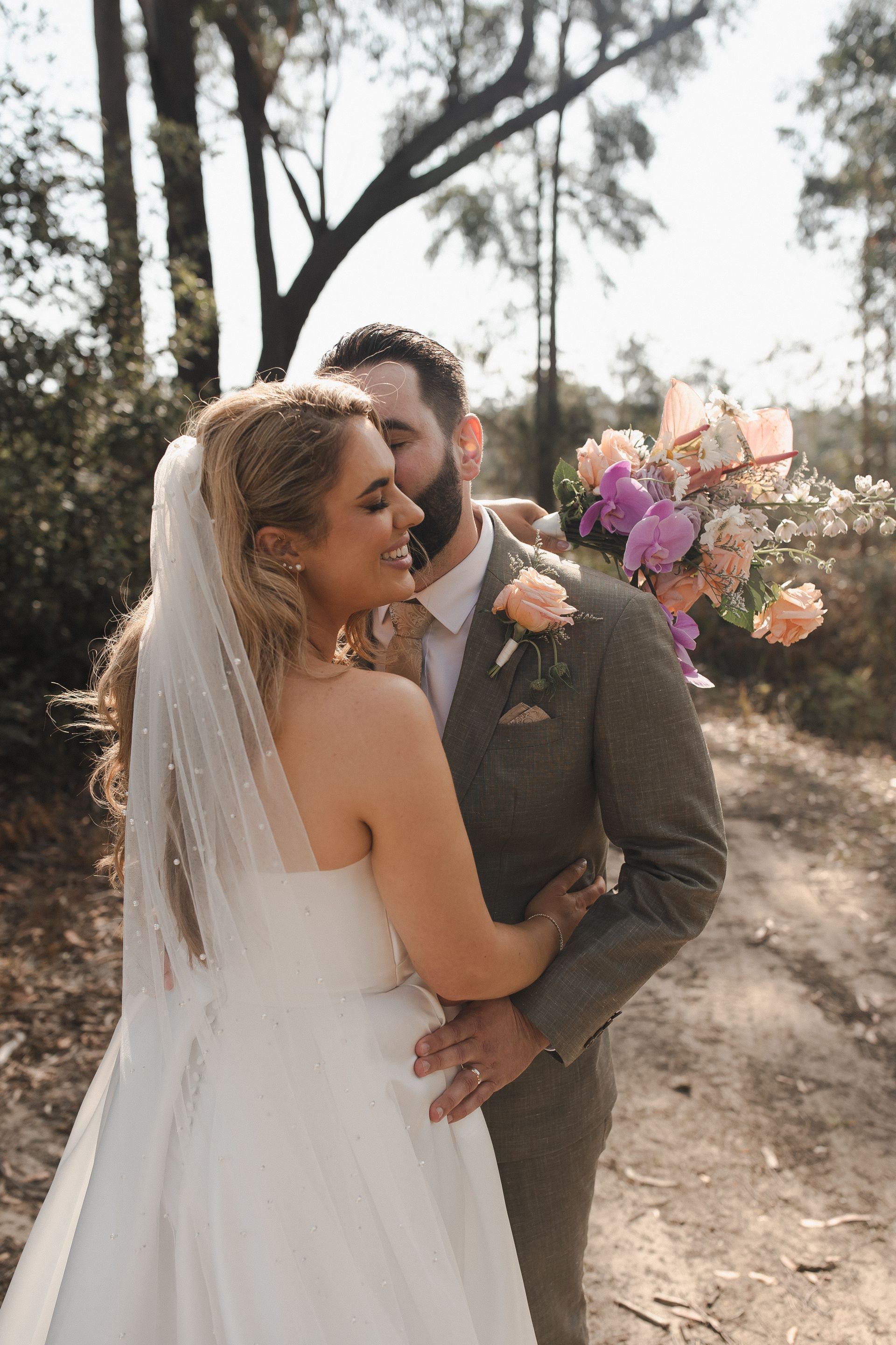 Bride and groom embracing outdoors, bride in white gown holding a colorful bouquet