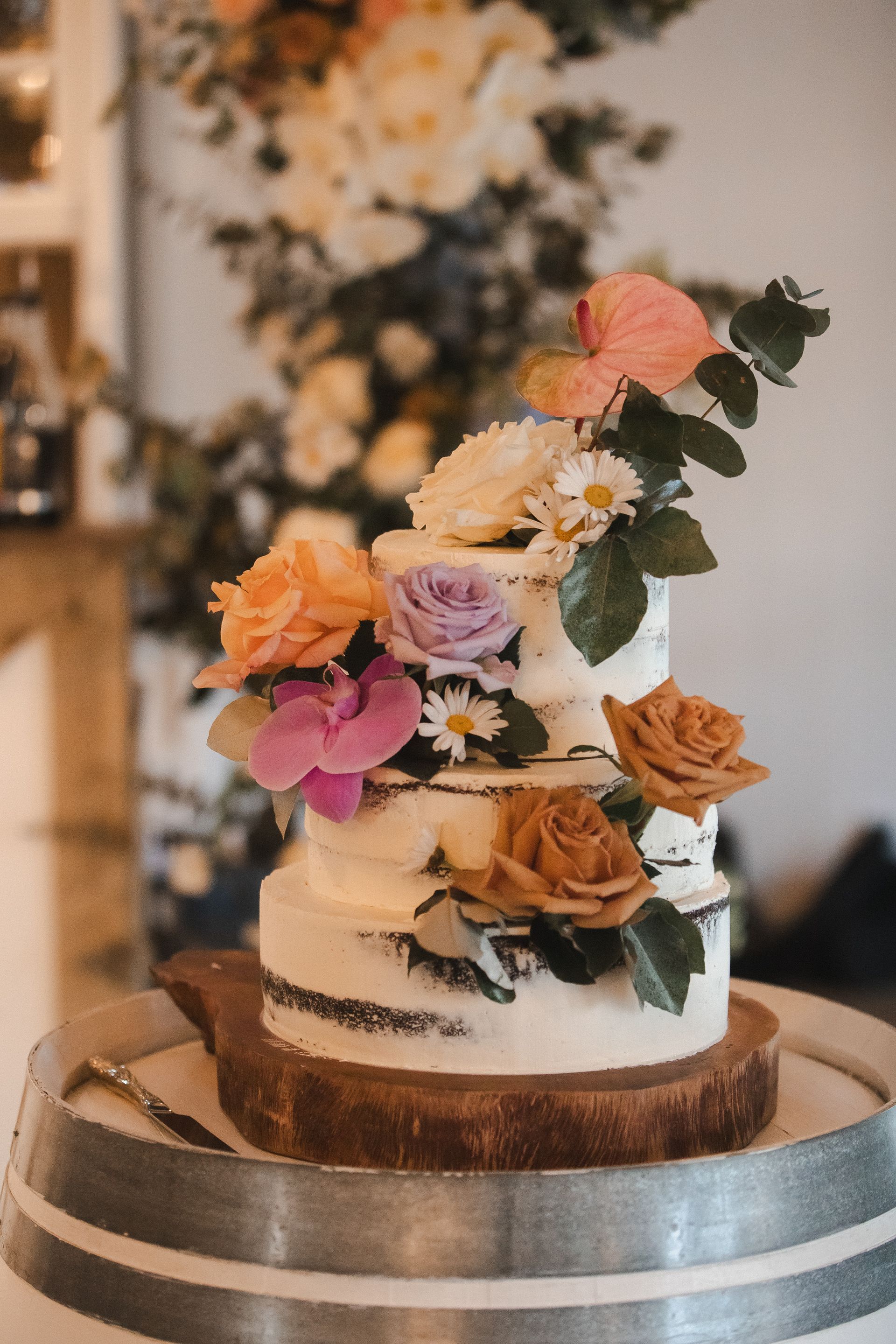 Two-tiered white cake with peach and pink flowers on a silver stand