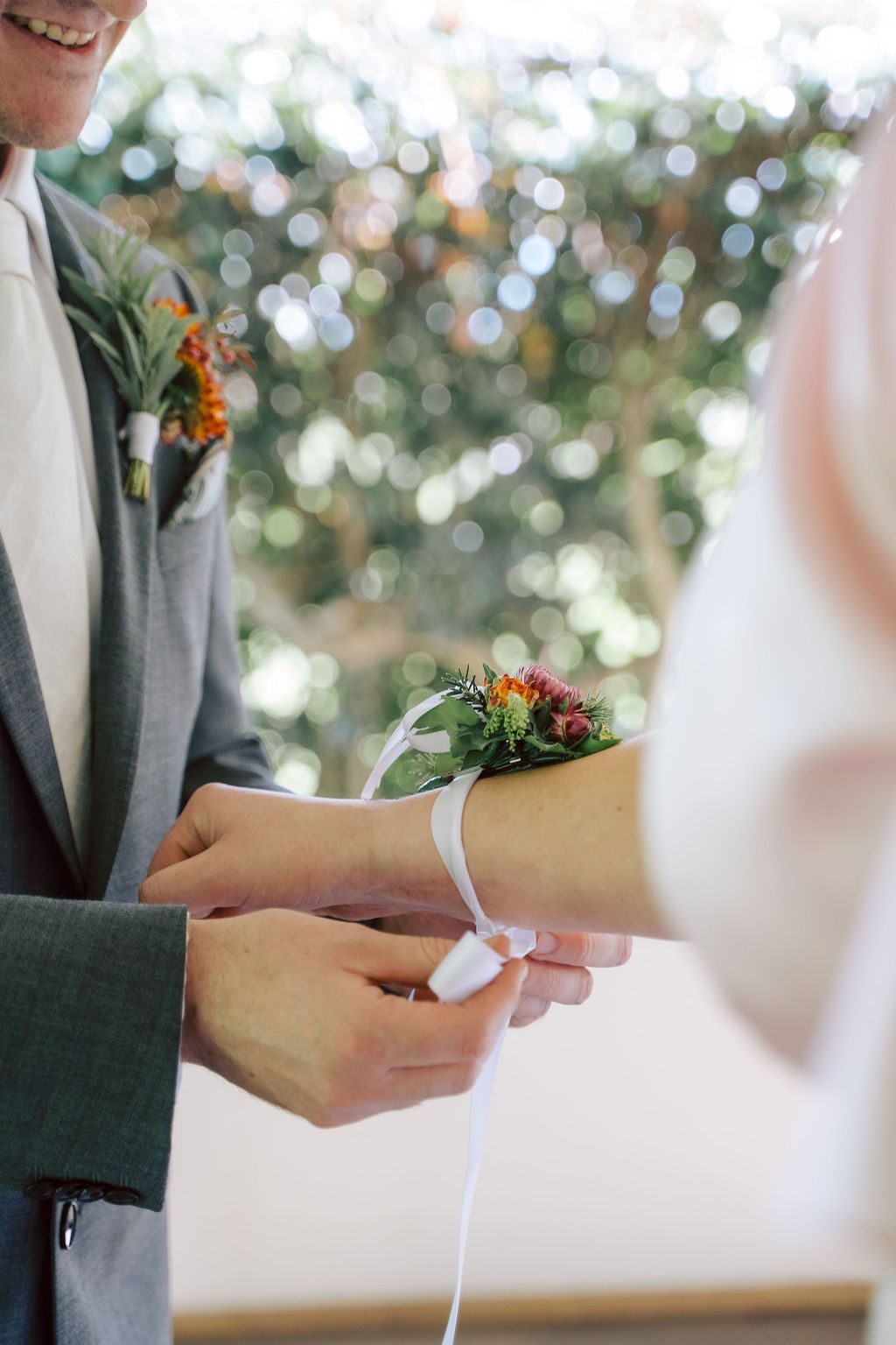 Groom fastening a white ribbon on the bride’s wrist during an outdoor wedding ceremony