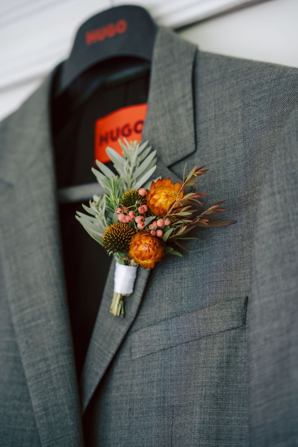 Gray suit jacket with orange boutonniere on a hanger