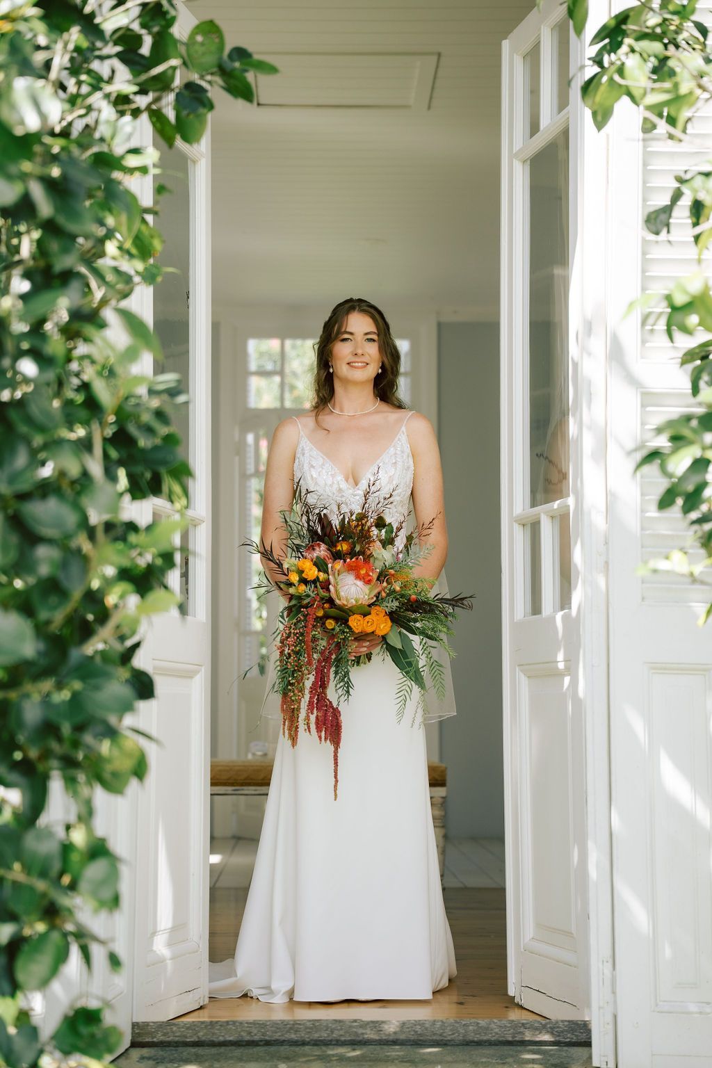 Woman in a white dress holding a colorful bouquet in a doorway framed by greenery