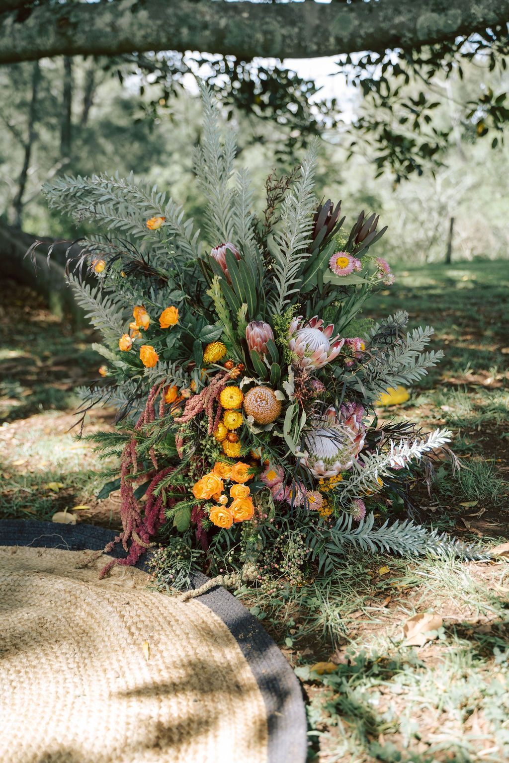 Rustic floral arrangement with orange, pink, and green blooms under a tree outdoors