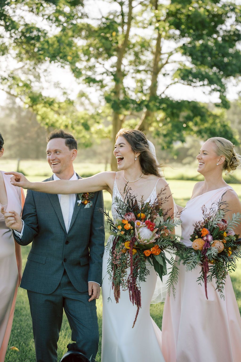 Wedding party walking outdoors, smiling and carrying colorful bouquets in formal attire.
