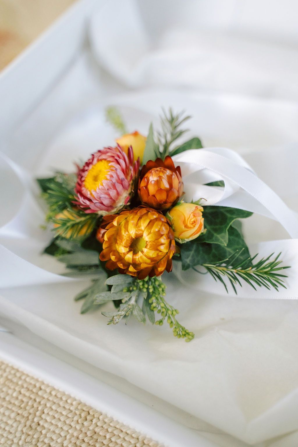 Small bouquet of orange and pink dried flowers with green foliage on a white plate