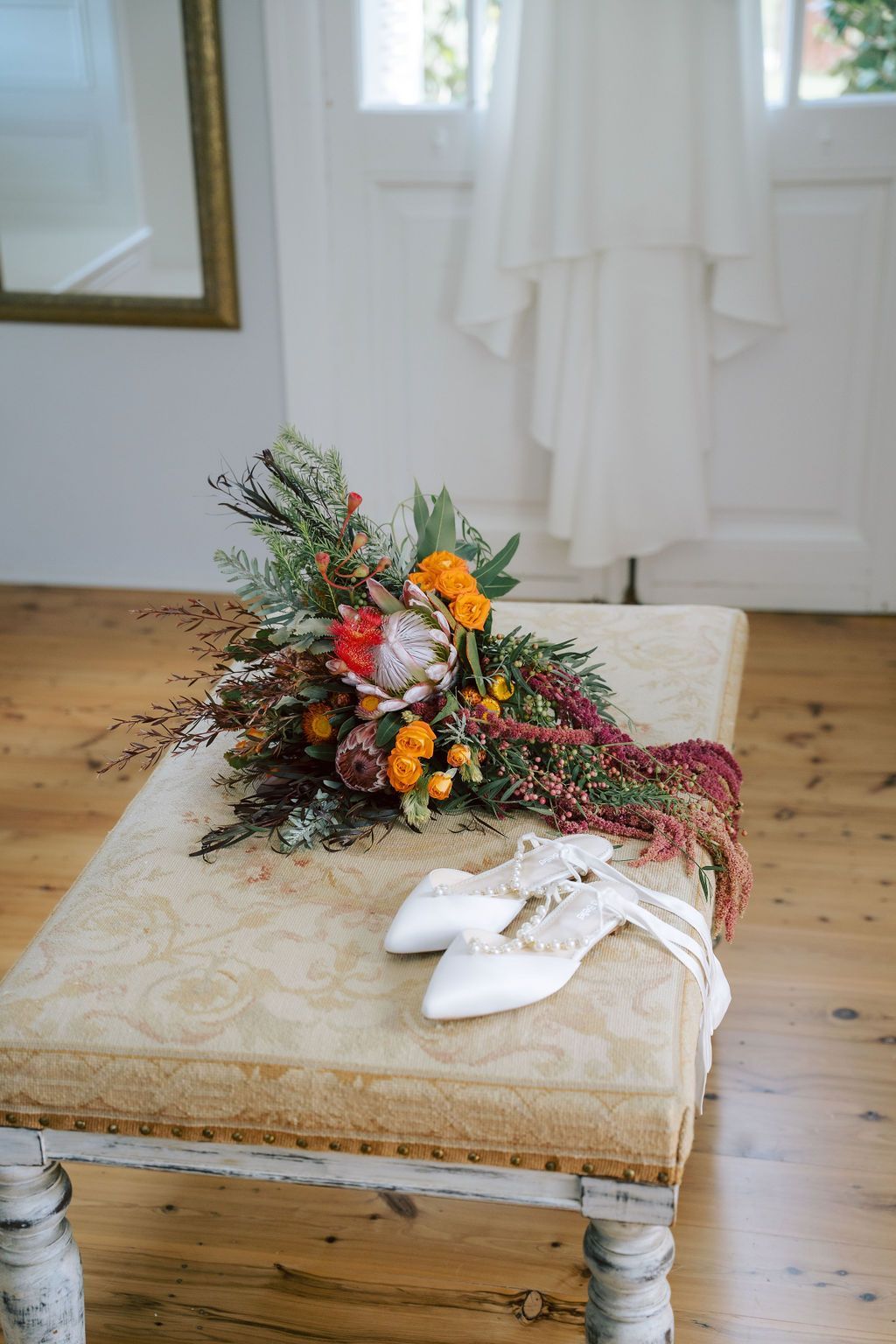 White shoes beside a colorful bouquet on a beige bench in a bright room