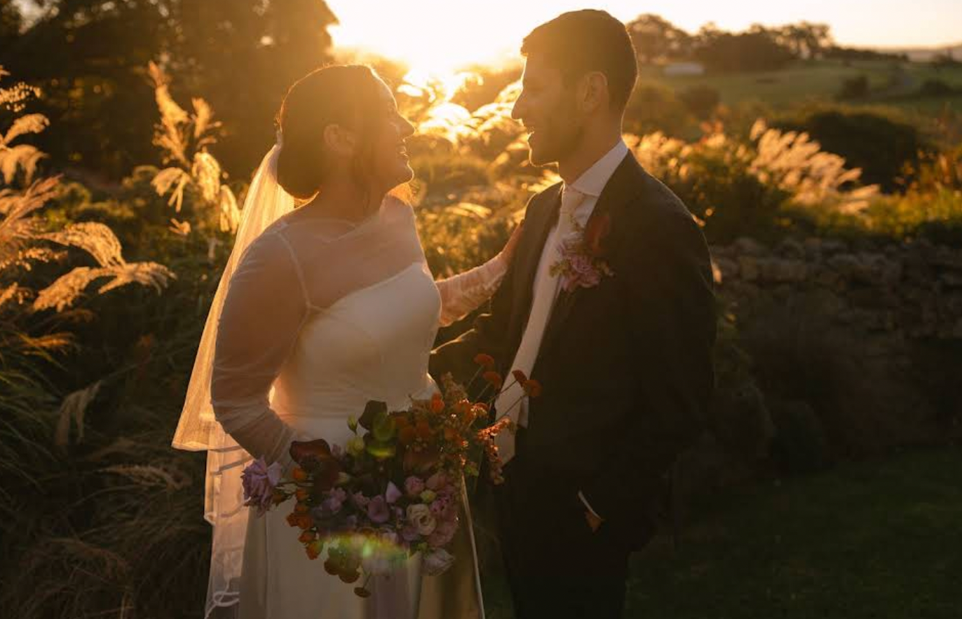 Sunset wedding couple standing in a garden, holding flowers and facing each other